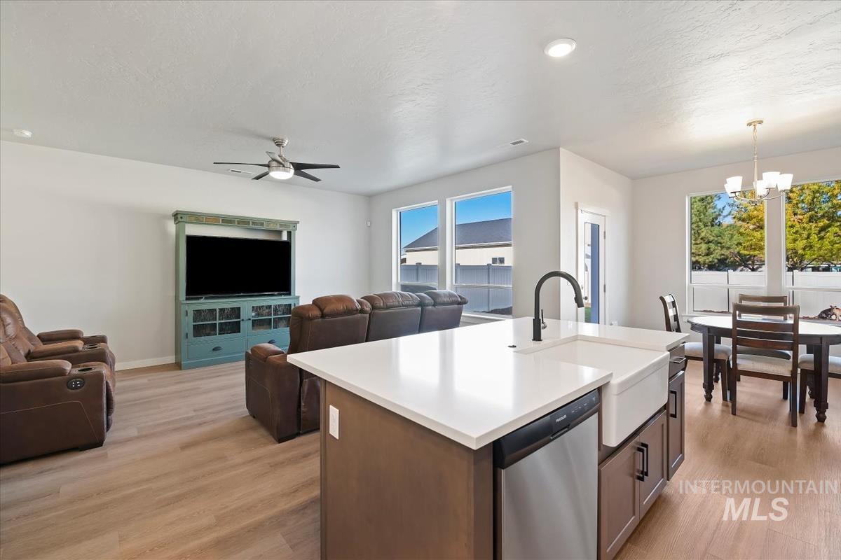 Kitchen with open floor plan, stainless steel dishwasher, light wood-type flooring, an island with sink, and a textured ceiling