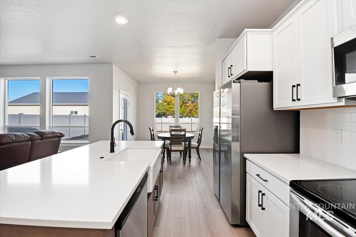 Kitchen with a center island with sink, light wood finished floors, decorative light fixtures, white cabinets, and appliances with stainless steel finishes