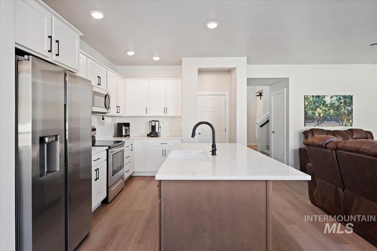 Kitchen with stainless steel appliances, decorative backsplash, an island with sink, light wood-type flooring, and open floor plan