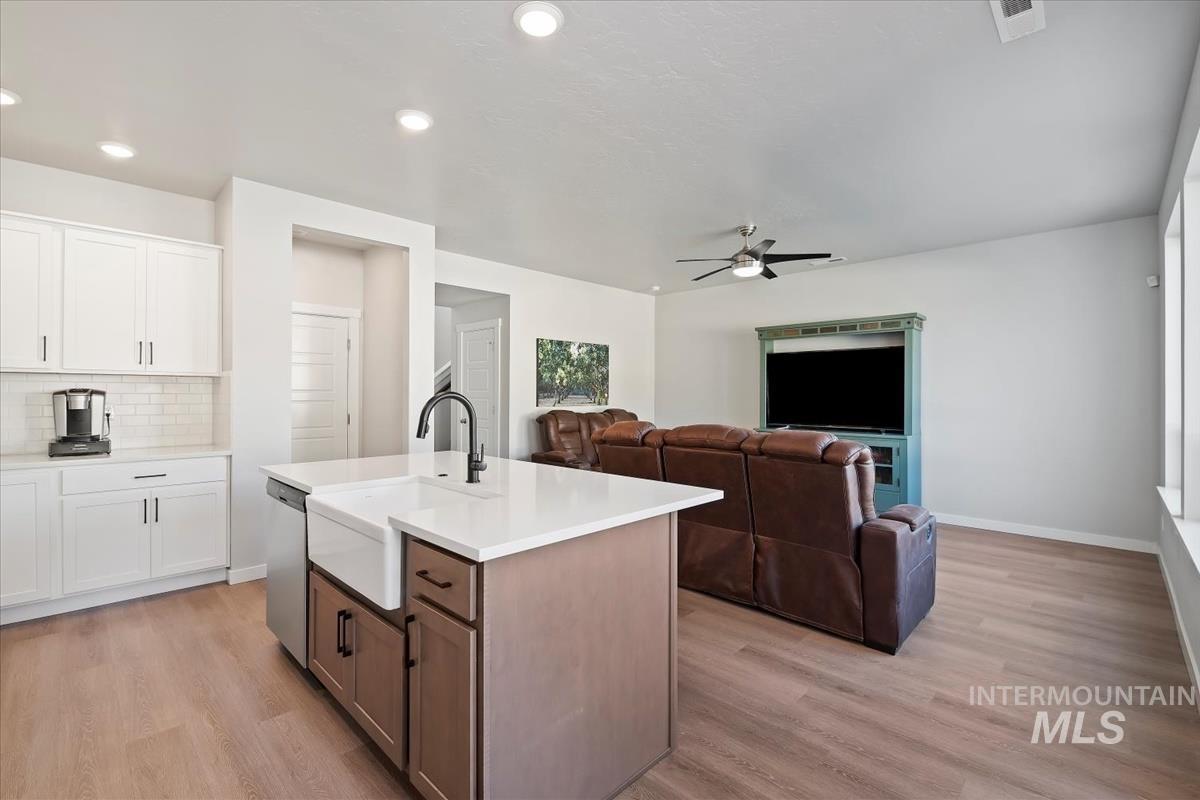 Kitchen featuring a kitchen island with sink, white cabinets, backsplash, light wood-type flooring, and open floor plan
