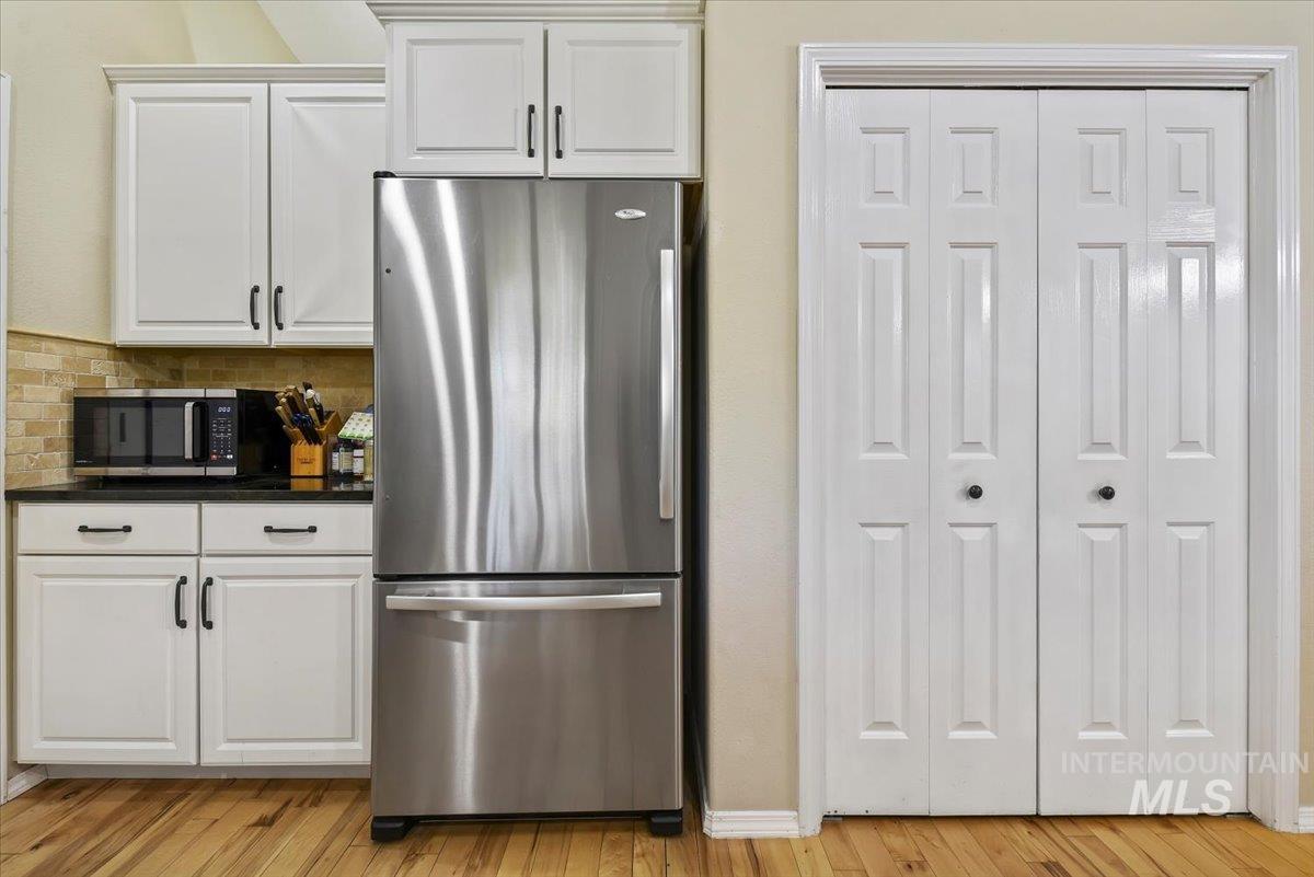 Kitchen with appliances with stainless steel finishes, white cabinetry, light wood-type flooring, and tasteful backsplash