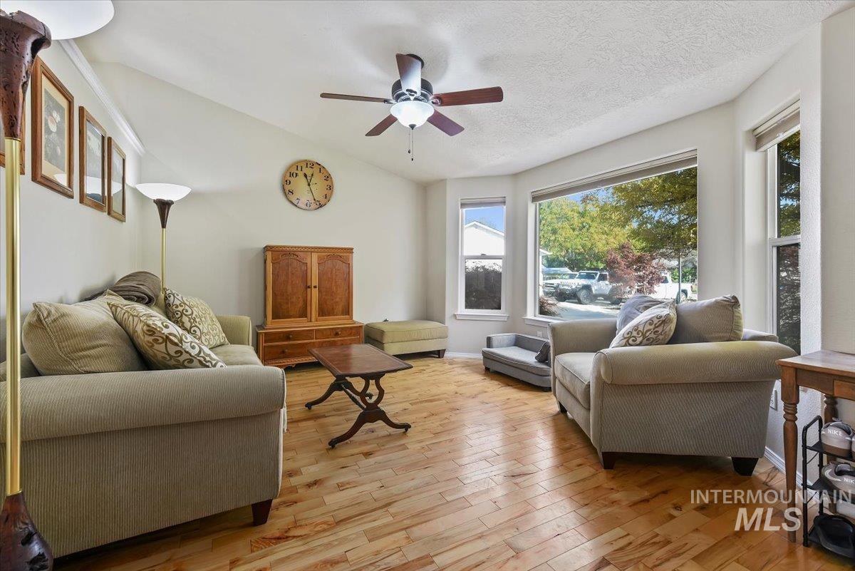 Living area with light wood-style floors, a ceiling fan, a textured ceiling, and vaulted ceiling