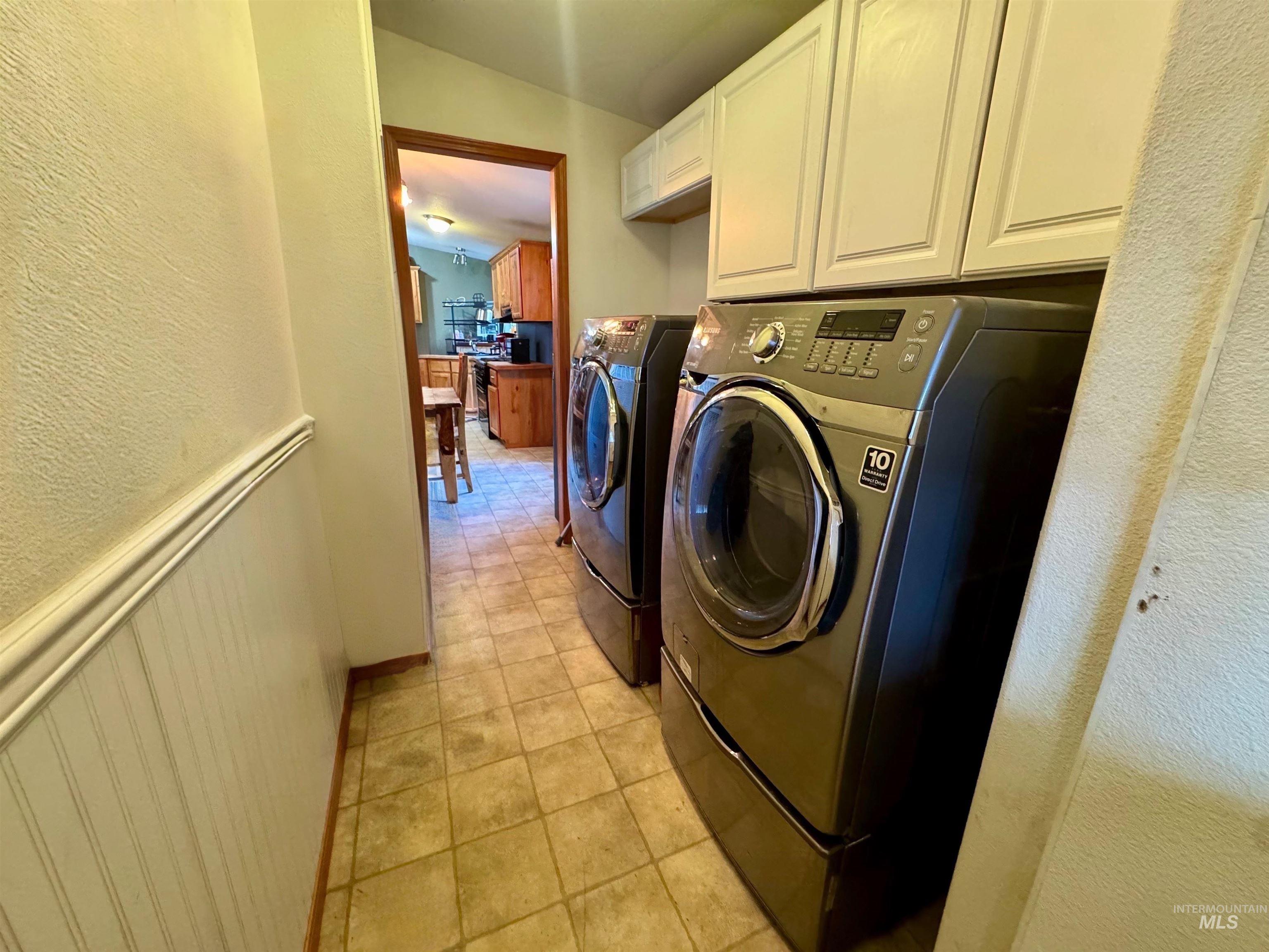 Laundry room with a textured wall, cabinet space, light tile patterned floors, washing machine and clothes dryer, and a wainscoted wall