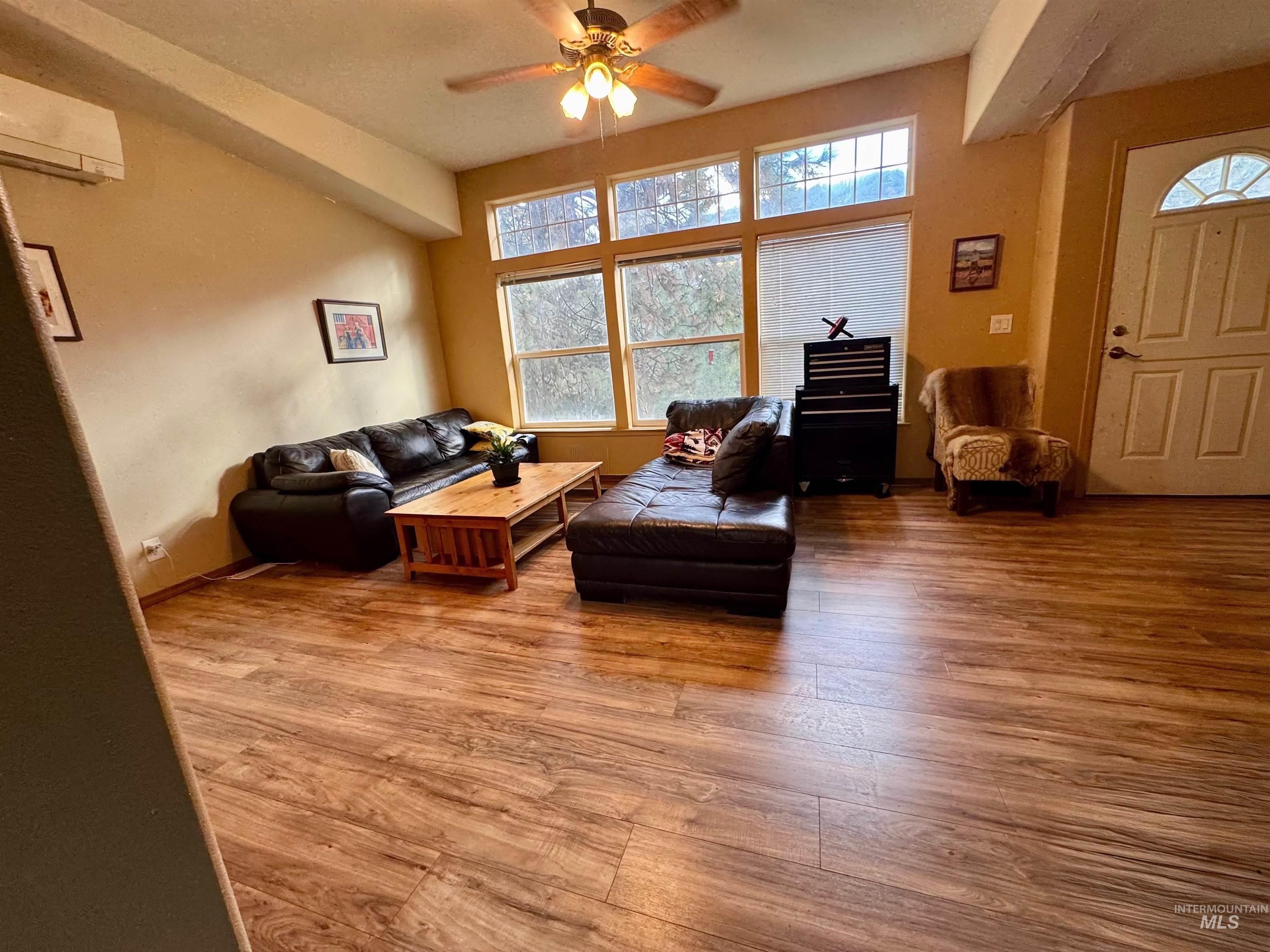 Living area with wood finished floors, a wall mounted AC, and a ceiling fan