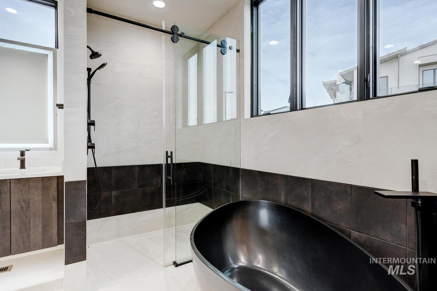 Full bathroom featuring a shower stall, a freestanding tub, vanity, and tile walls