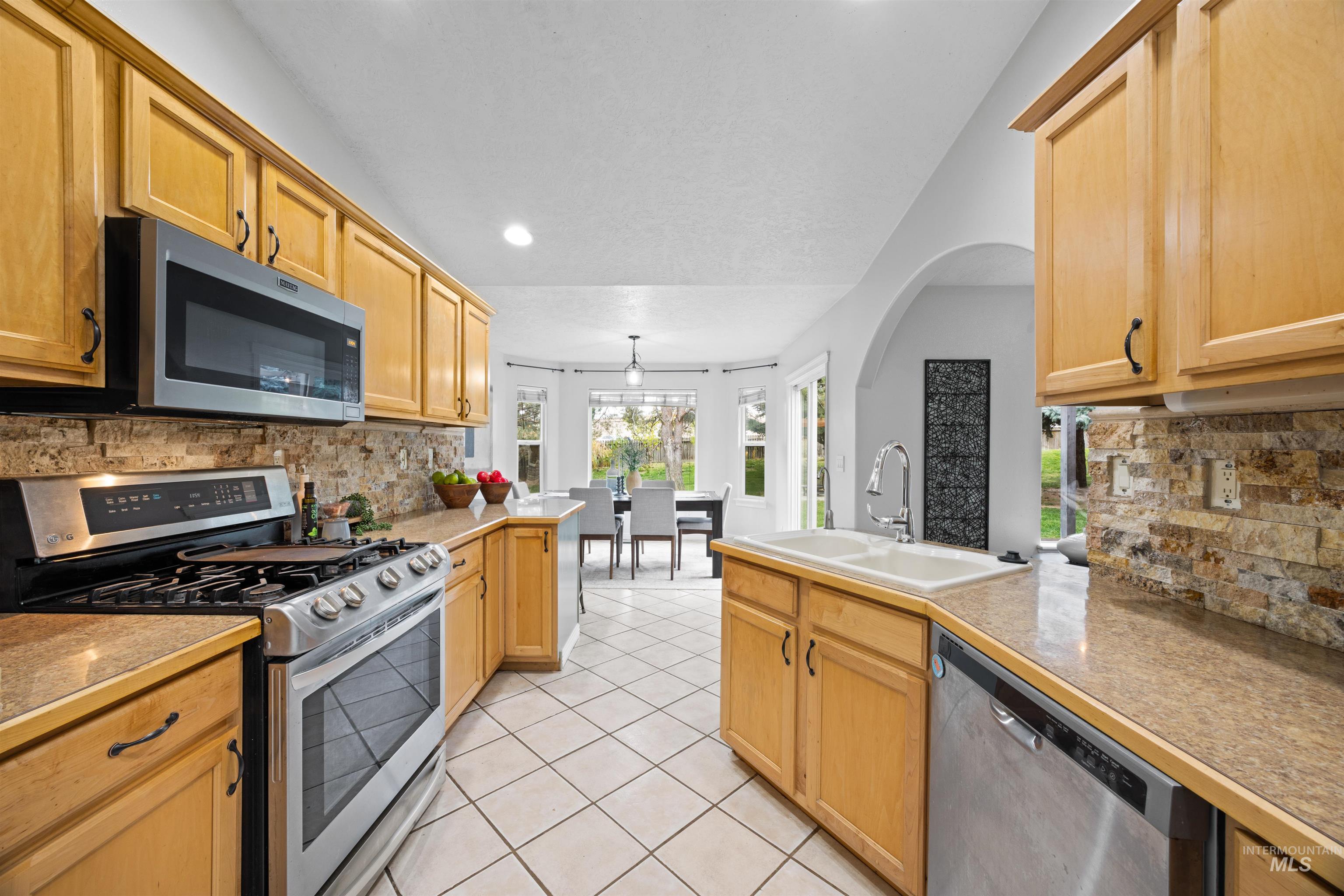 Kitchen with tasteful backsplash, stainless steel appliances, a peninsula, light tile patterned flooring, and recessed lighting