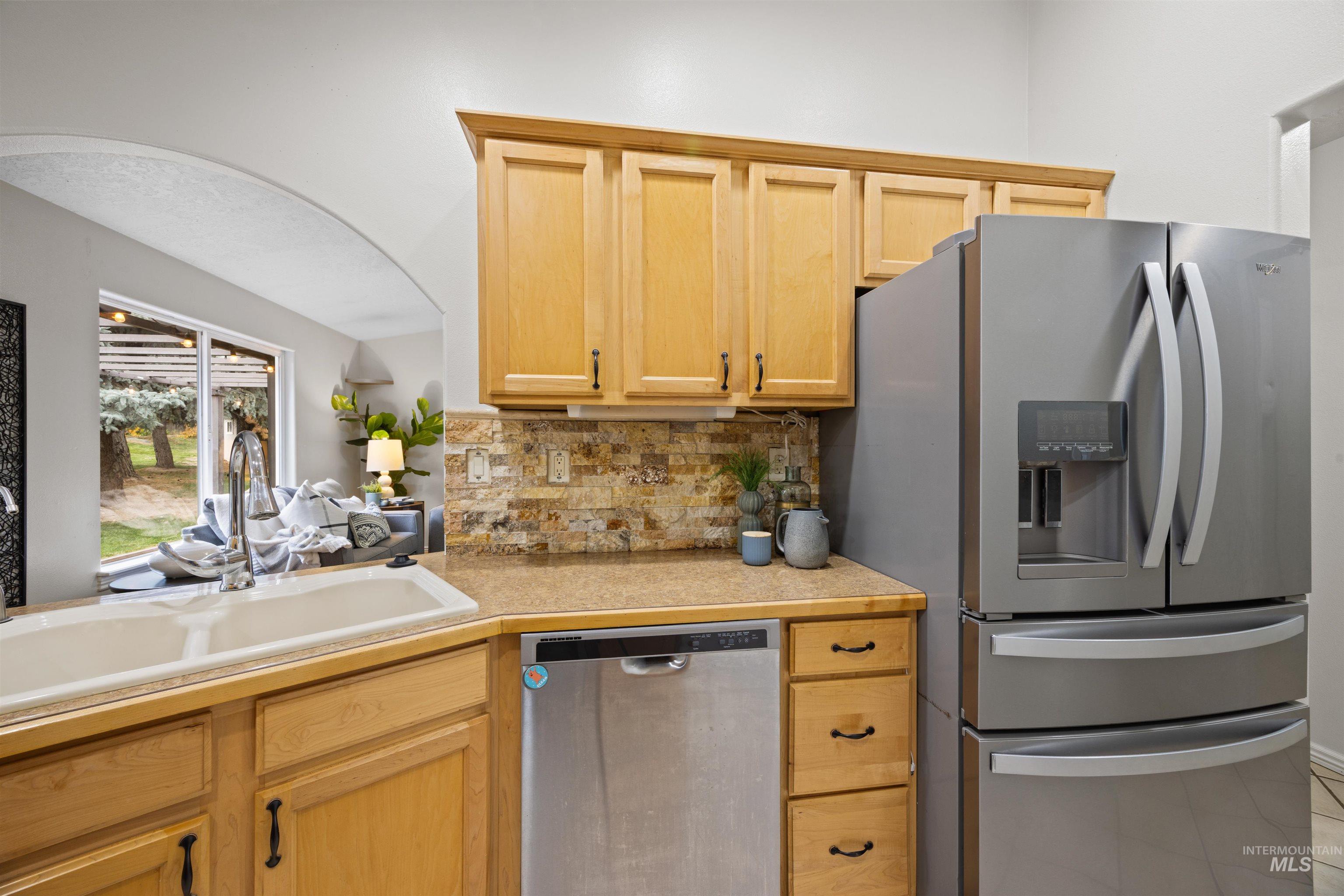 Kitchen featuring stainless steel appliances, light countertops, tasteful backsplash, light brown cabinetry, and light tile patterned floors