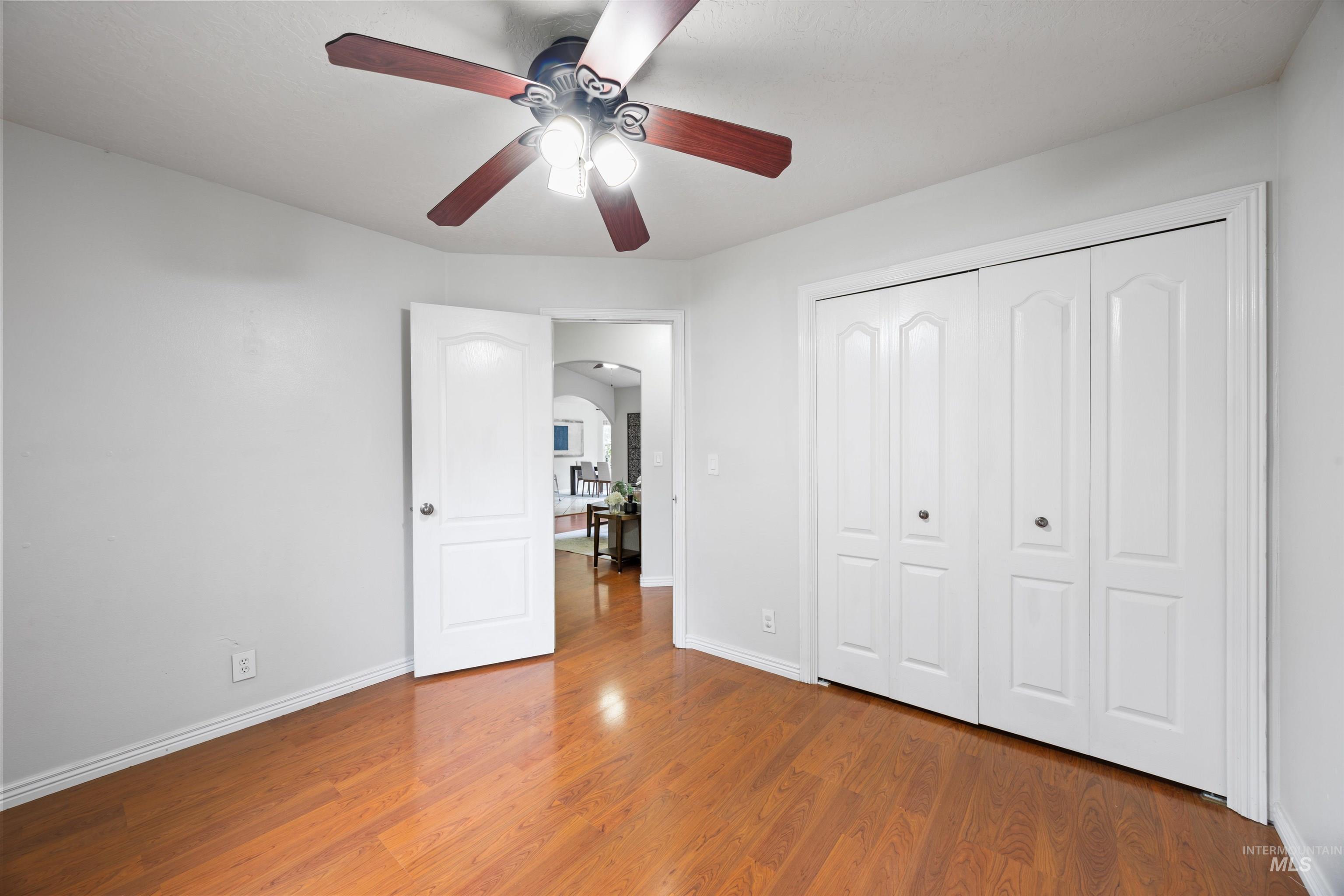 Unfurnished bedroom featuring wood finished floors, arched walkways, ceiling fan, and a closet