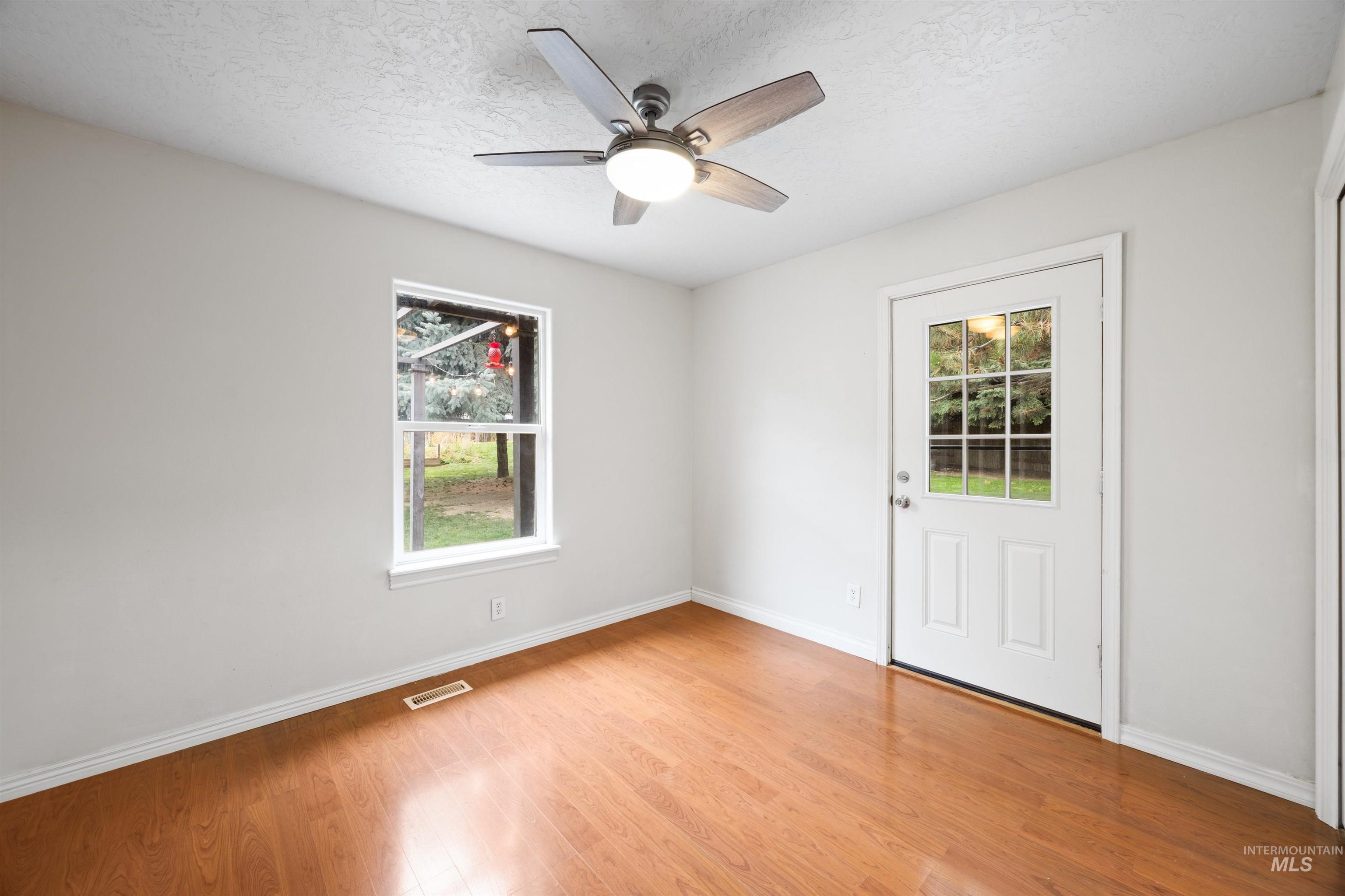Empty room with a textured ceiling, light wood-type flooring, and a ceiling fan