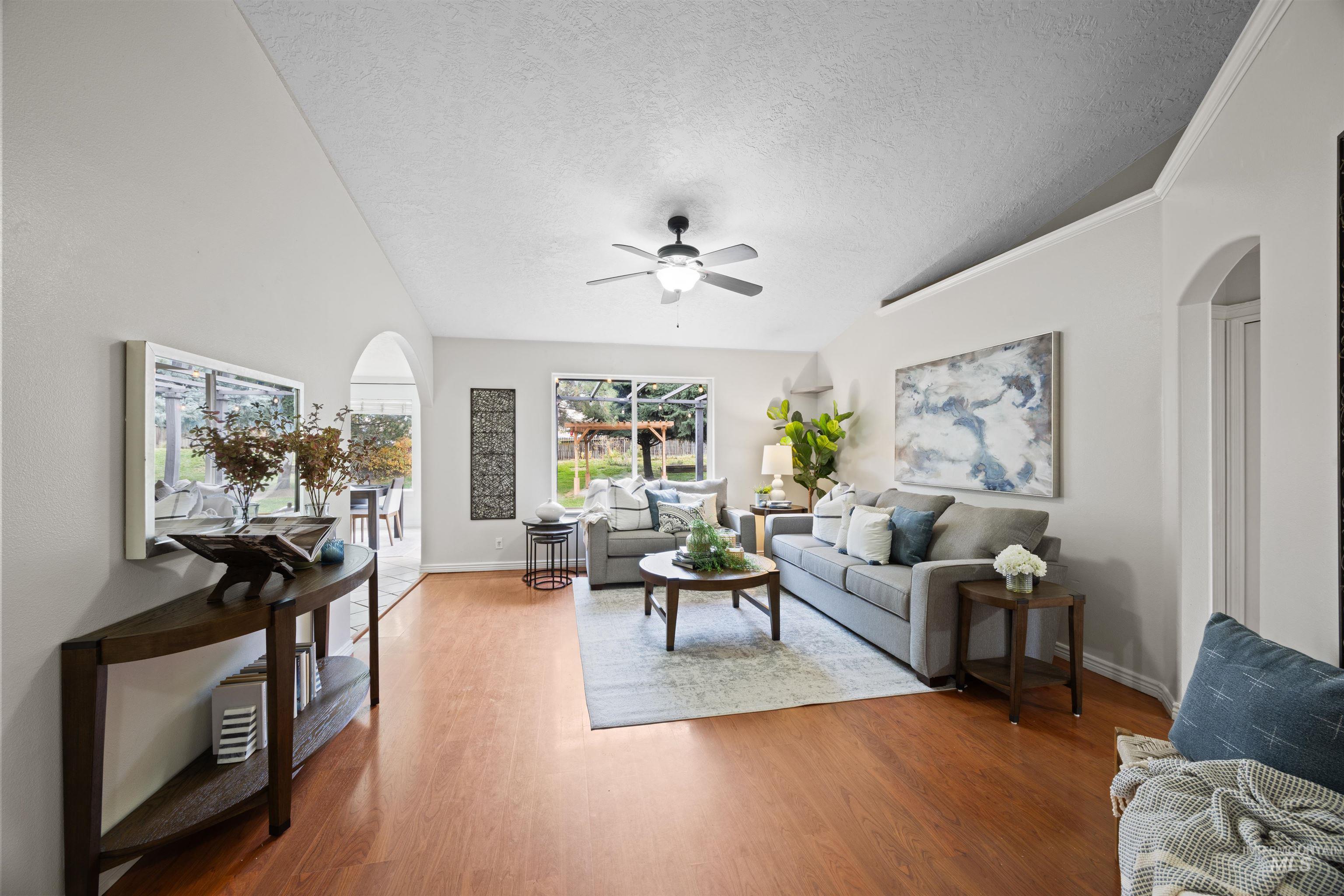 Living room with arched walkways, light wood finished floors, a textured ceiling, and ceiling fan