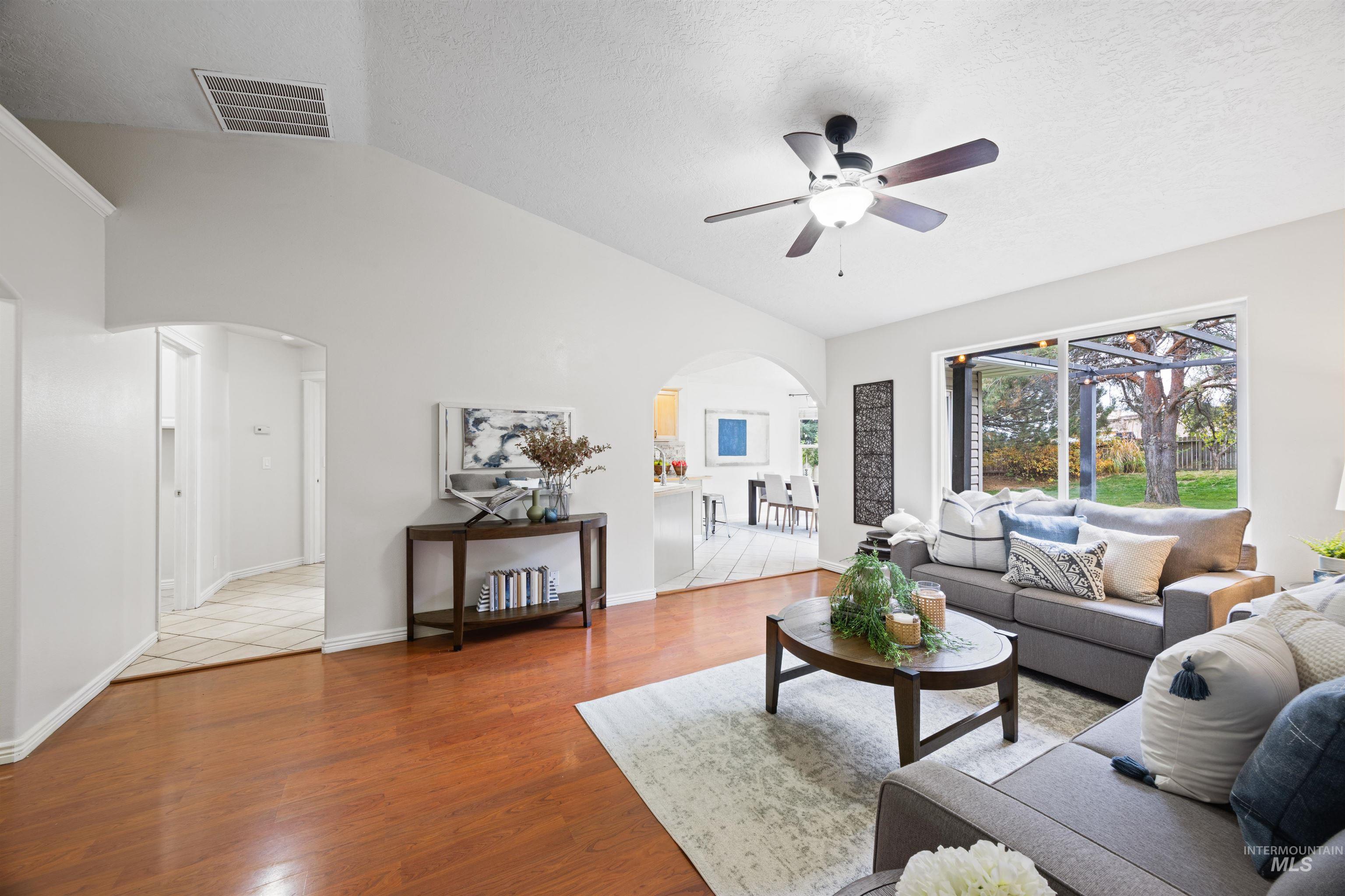 Living room with lofted ceiling, arched walkways, light wood finished floors, a textured ceiling, and ceiling fan