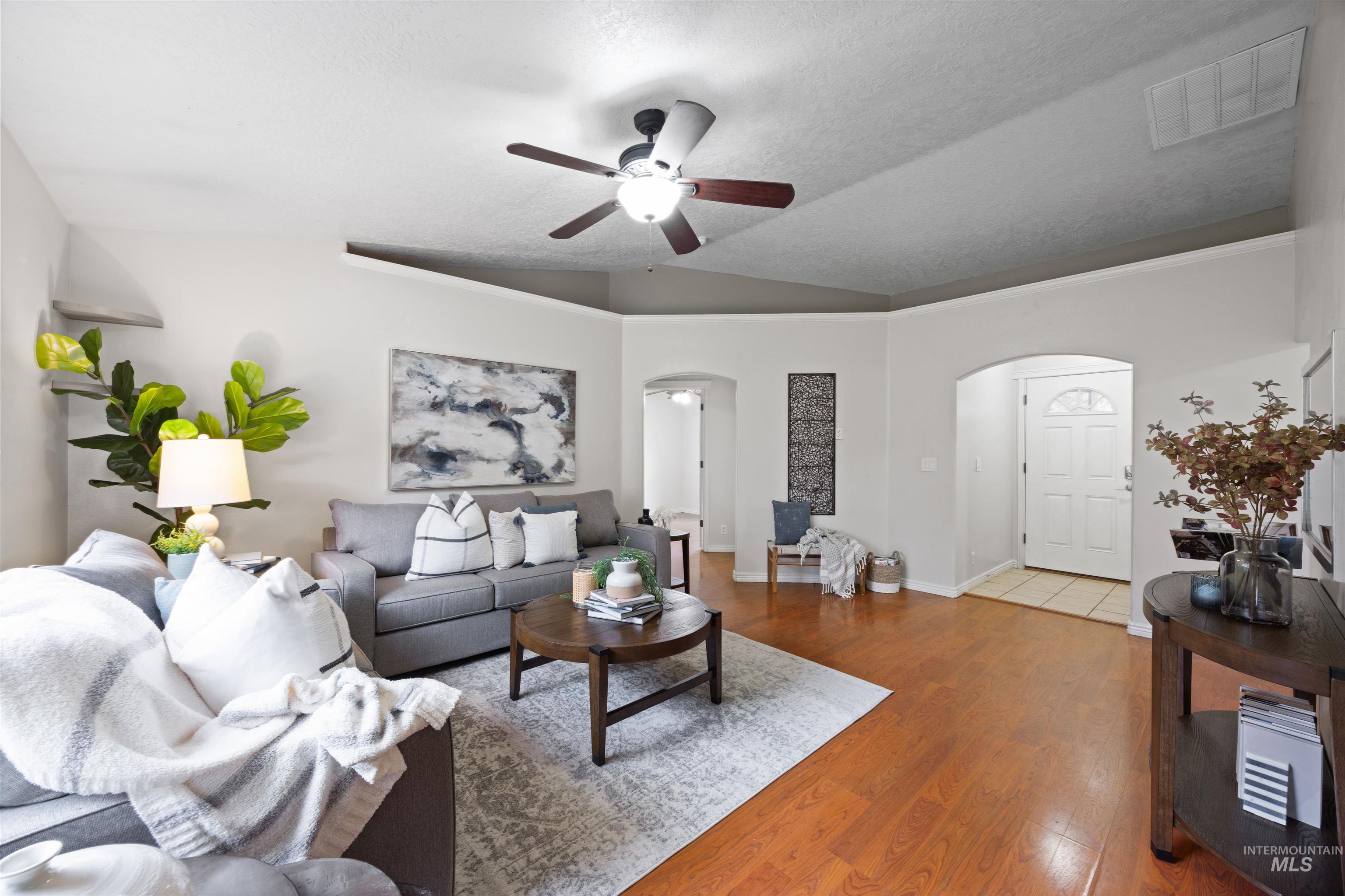 Living area with wood finished floors, vaulted ceiling, arched walkways, a textured ceiling, and ceiling fan