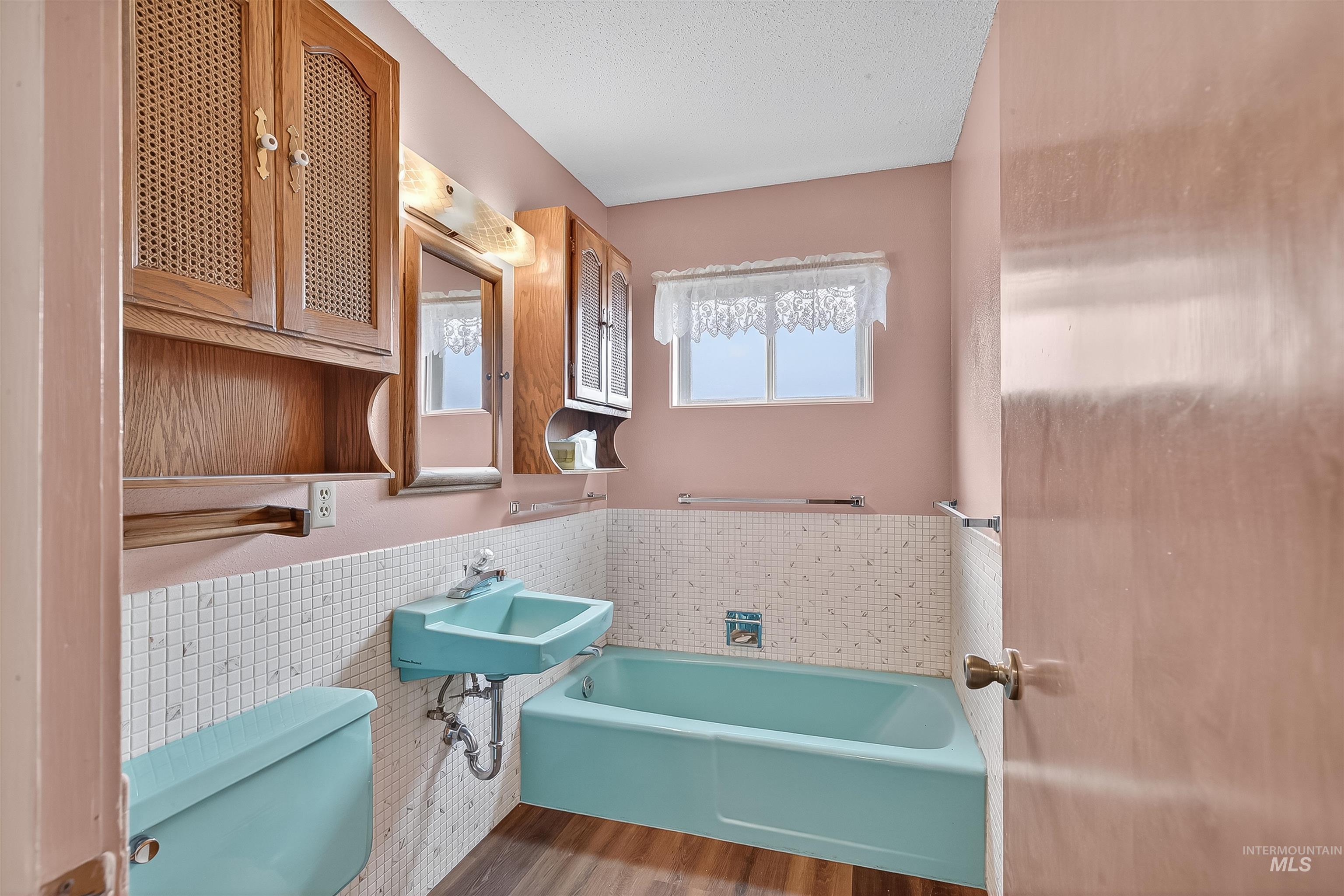 Bathroom with tile walls, a wainscoted wall, a garden tub, wood finished floors, and a textured ceiling