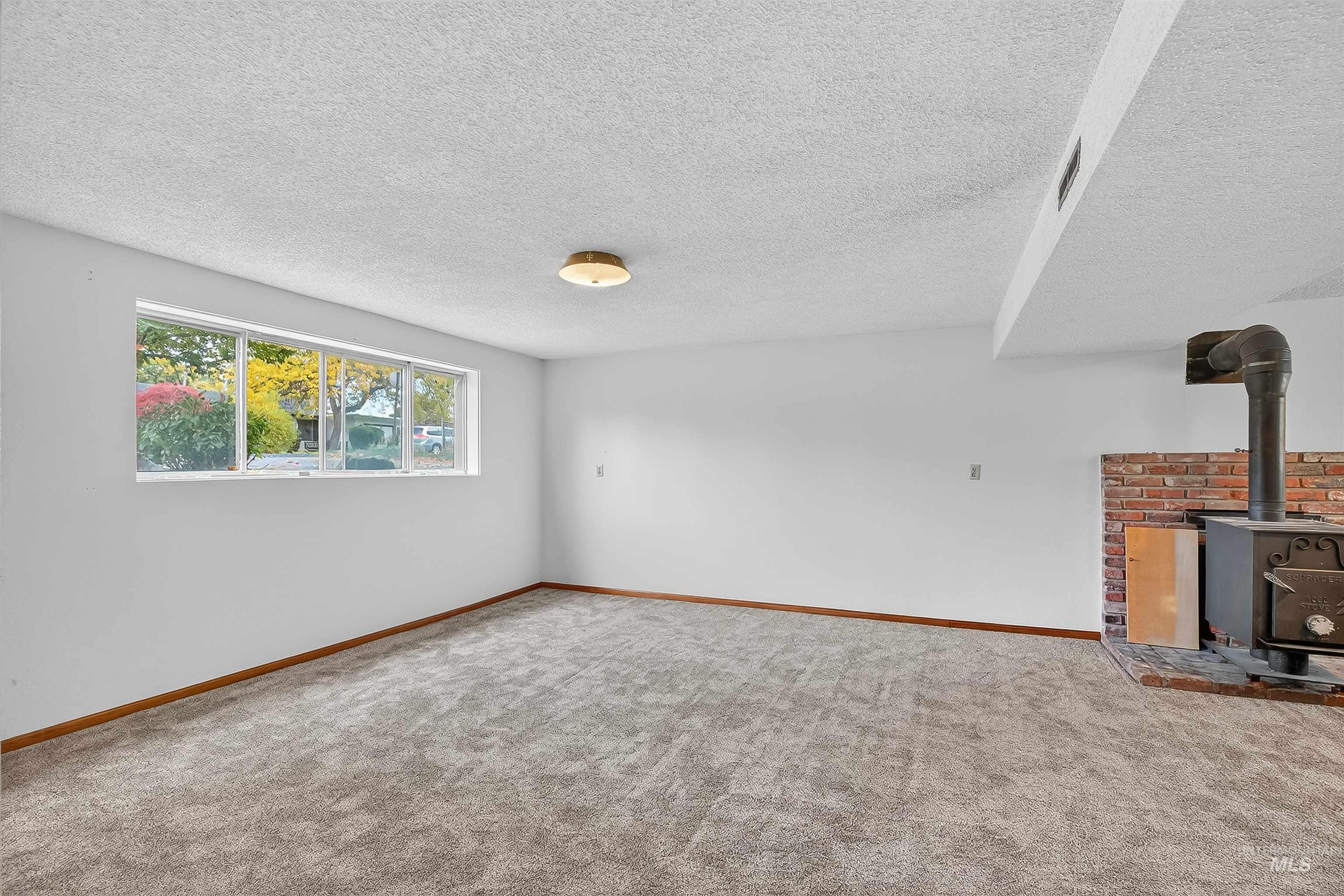 Unfurnished living room featuring a textured ceiling, carpet floors, and a wood stove