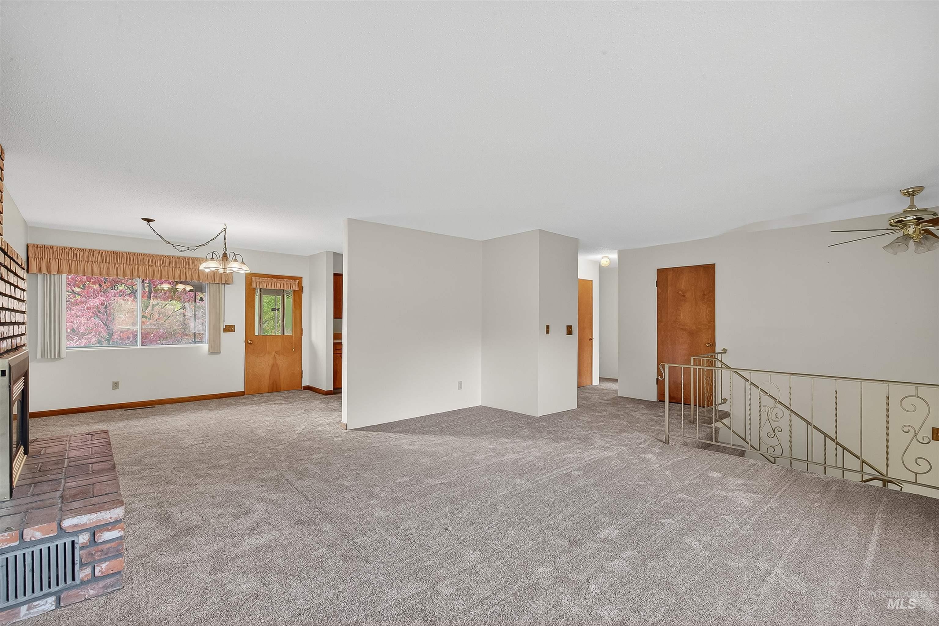 Unfurnished living room with a brick fireplace, a chandelier, carpet flooring, and a ceiling fan