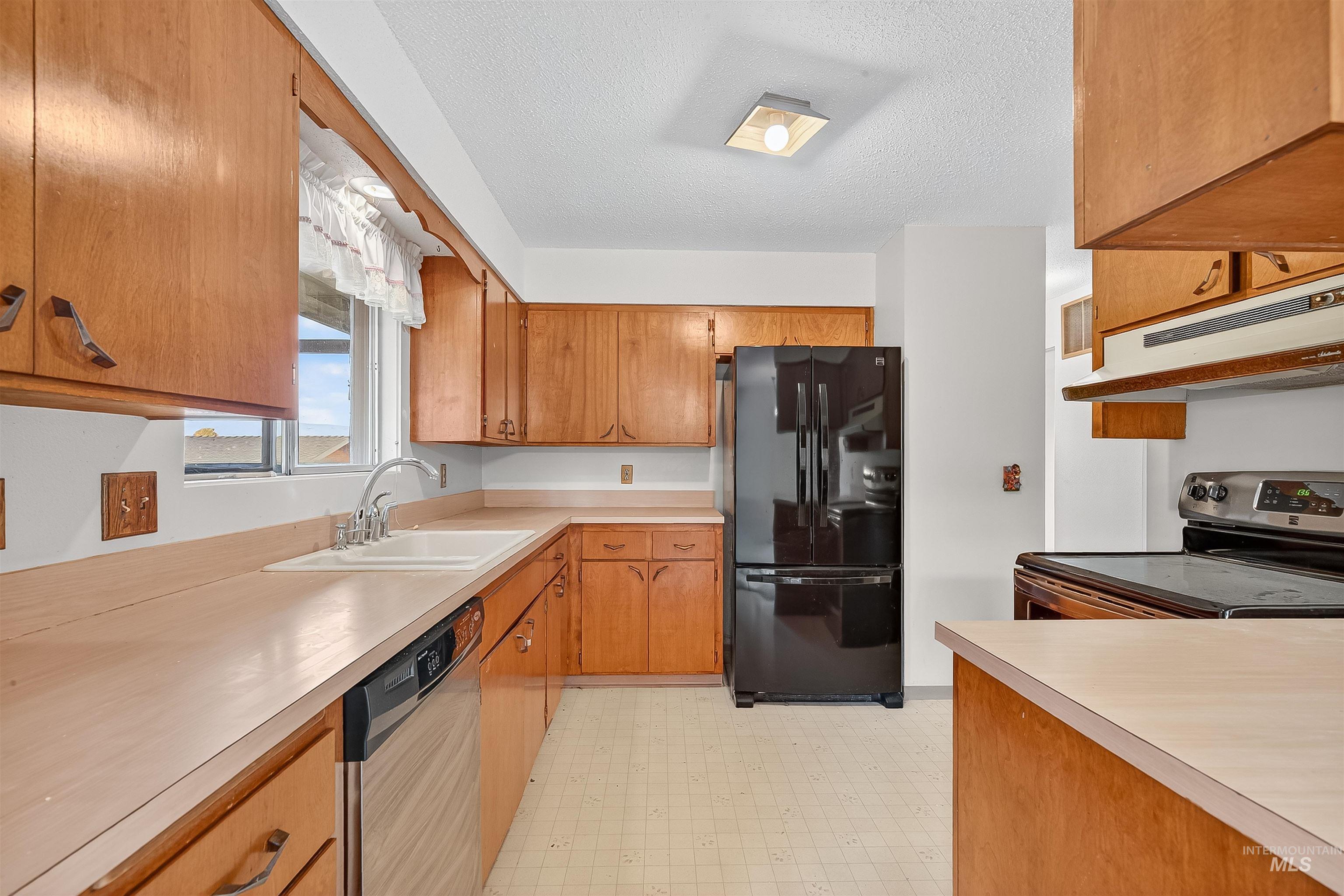 Kitchen with appliances with stainless steel finishes, brown cabinets, light floors, light countertops, and a textured ceiling