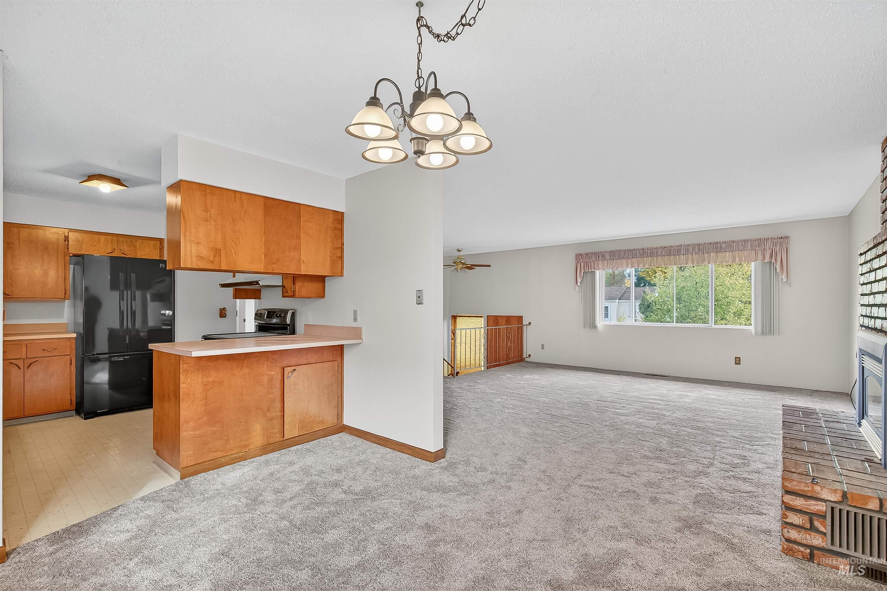 Kitchen featuring open floor plan, light countertops, brown cabinets, pendant lighting, and freestanding refrigerator