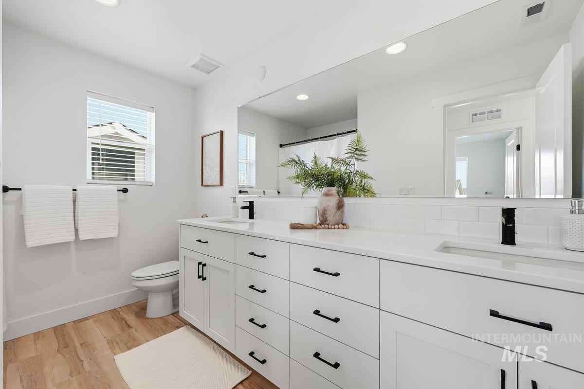 Full bathroom featuring double vanity, a shower with shower curtain, light wood-type flooring, recessed lighting, and decorative backsplash