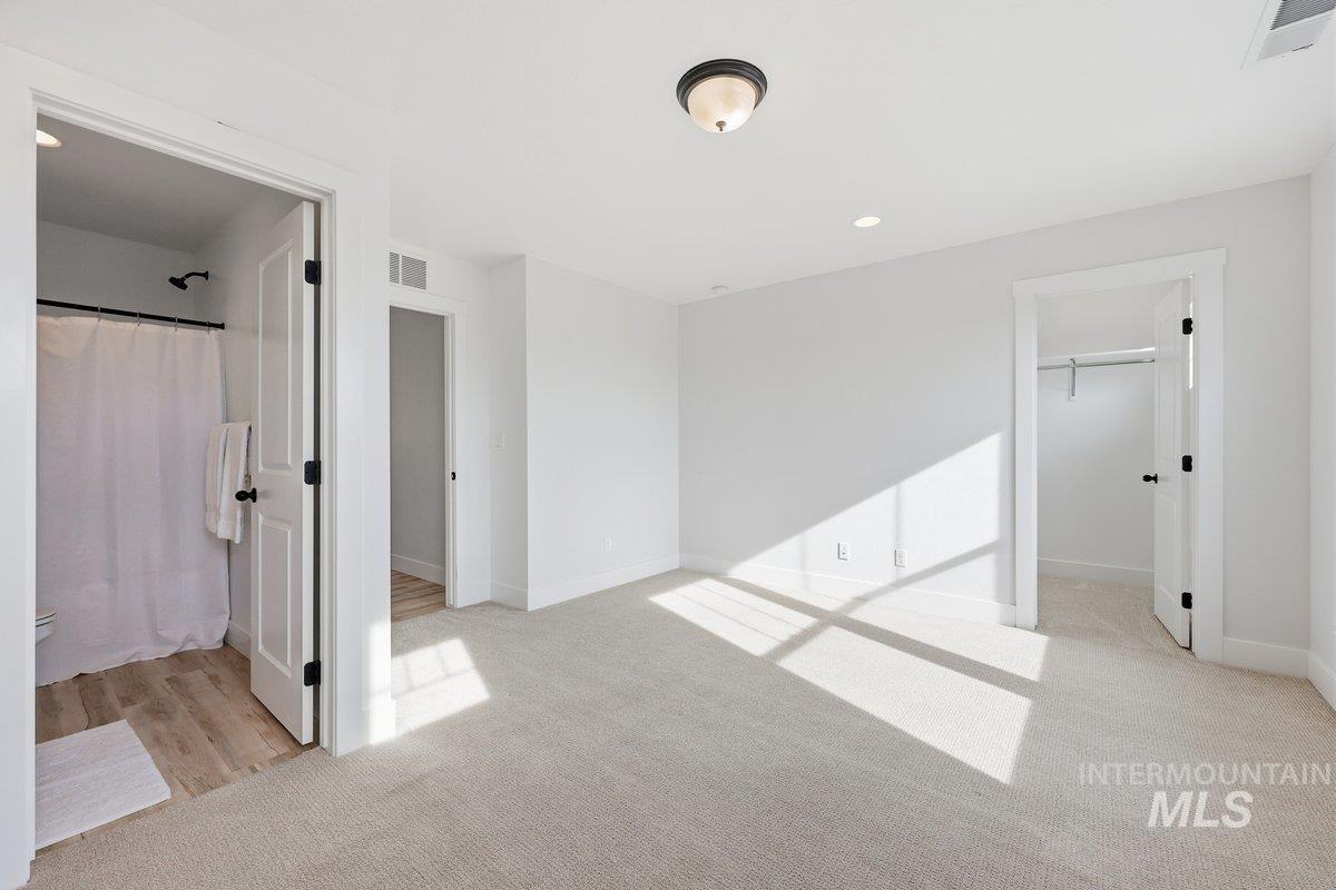 Unfurnished bedroom with a spacious closet, recessed lighting, light carpet, and ensuite bath