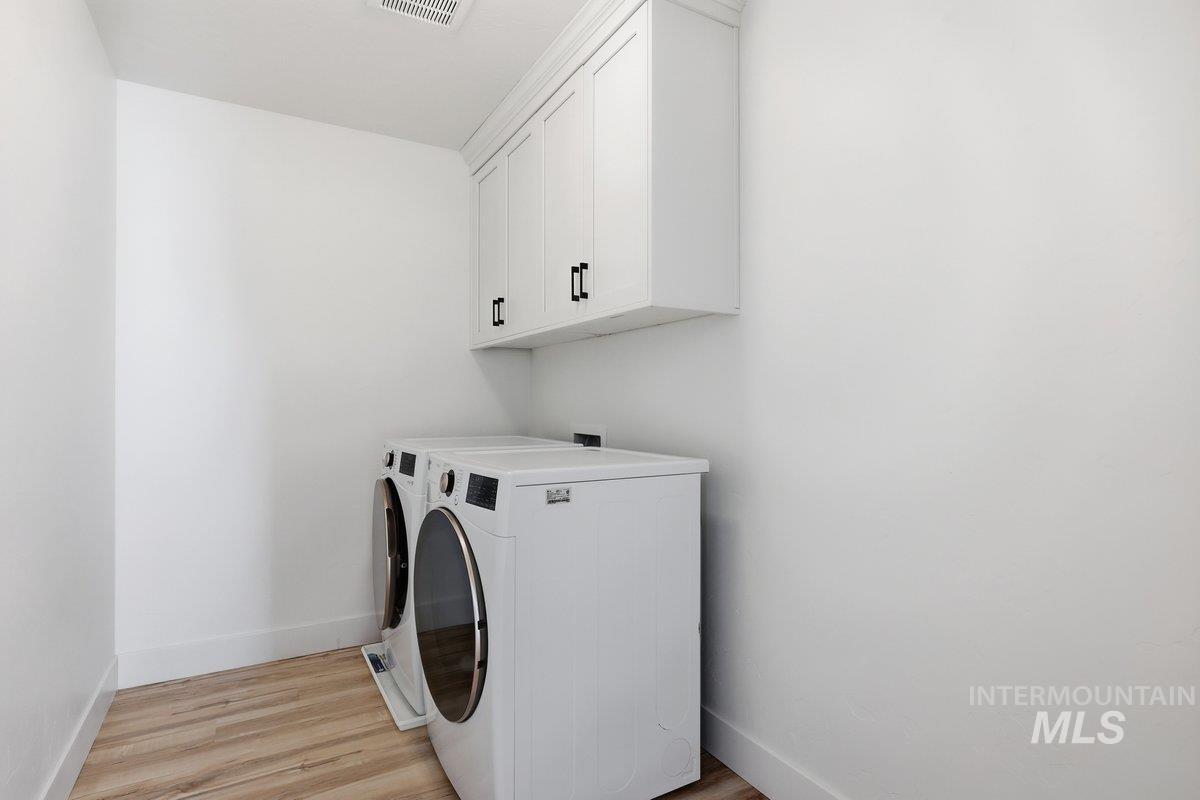 Washroom featuring light wood-style flooring, cabinet space, and washer and clothes dryer