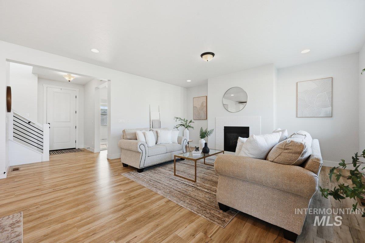 Living room featuring light wood-type flooring, a brick fireplace, stairs, and recessed lighting