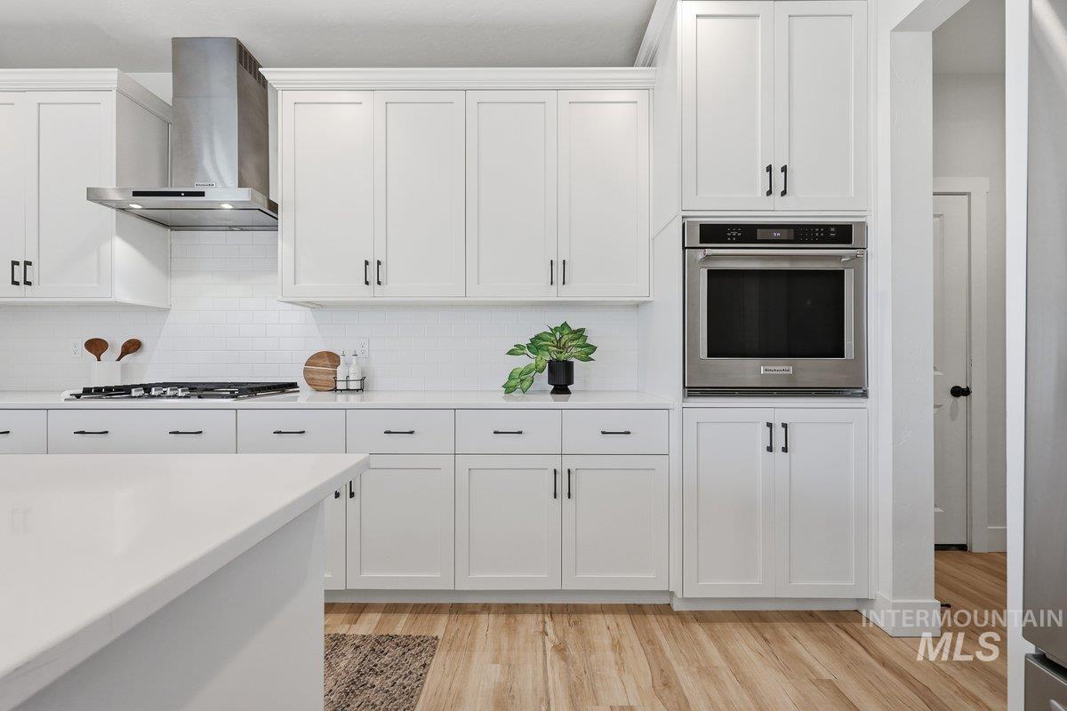 Kitchen with stainless steel appliances, wall chimney exhaust hood, light wood-type flooring, white cabinetry, and tasteful backsplash