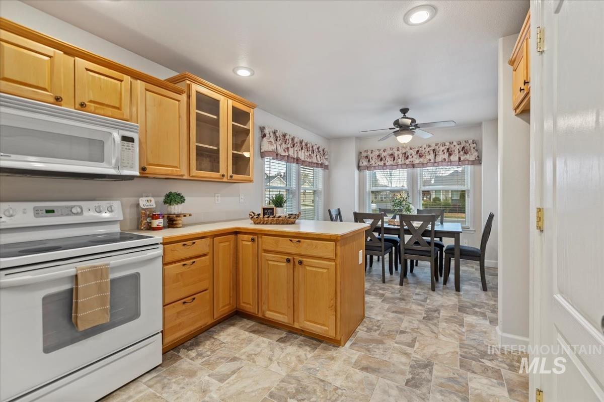 Kitchen with white appliances, glass insert cabinets, light countertops, recessed lighting, and stone finish floors