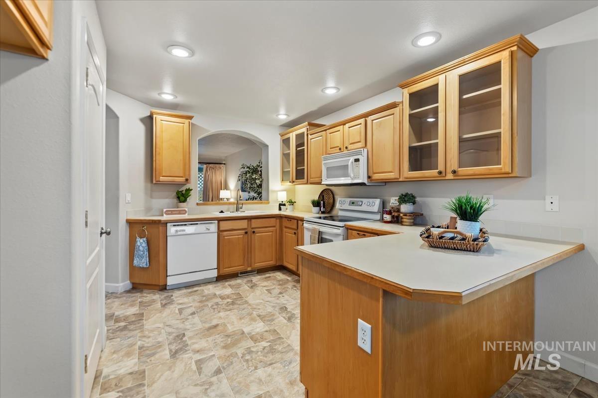 Kitchen featuring glass insert cabinets, light countertops, white appliances, a peninsula, and a kitchen breakfast bar