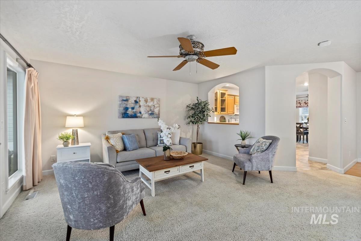 Living area featuring arched walkways, carpet floors, a textured ceiling, and ceiling fan