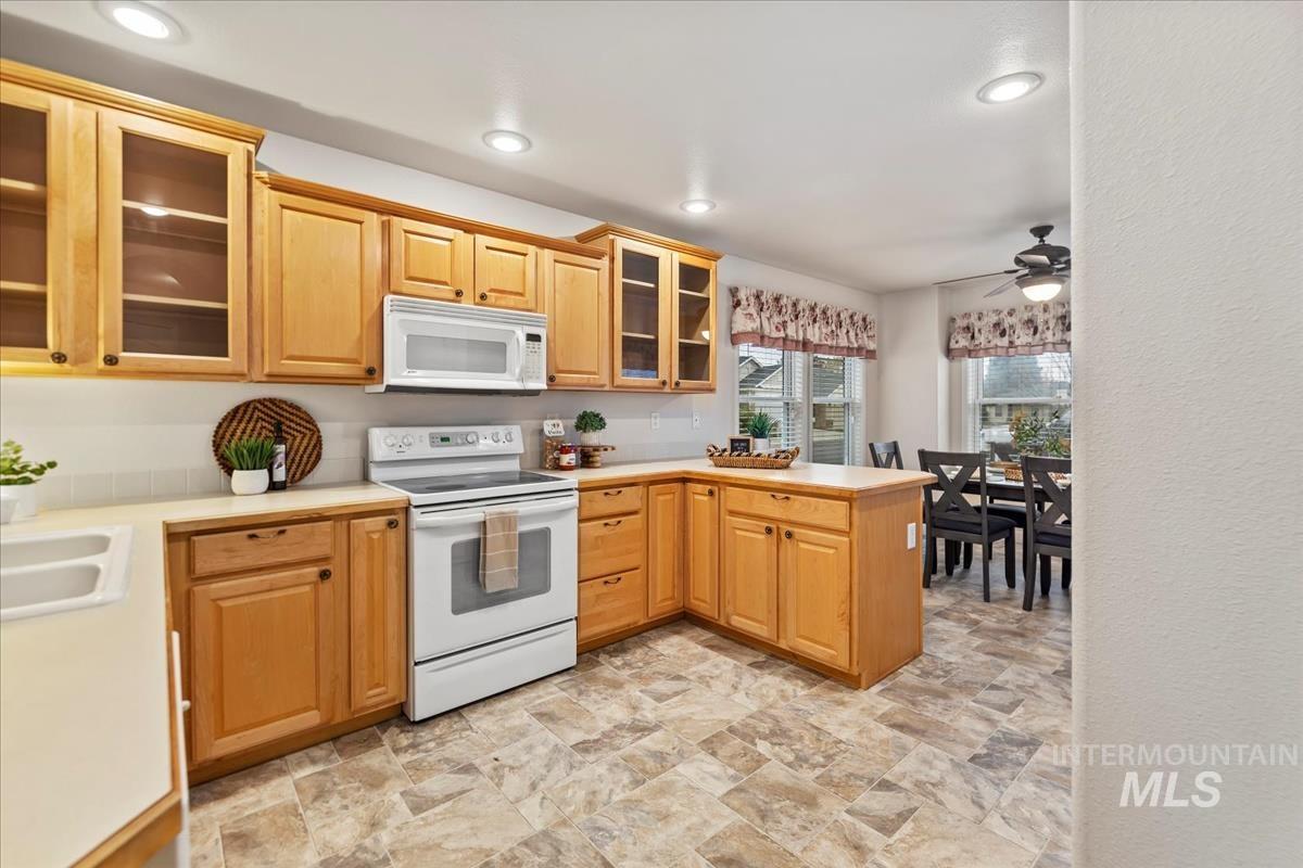 Kitchen featuring glass insert cabinets, white appliances, light countertops, a peninsula, and stone finish flooring