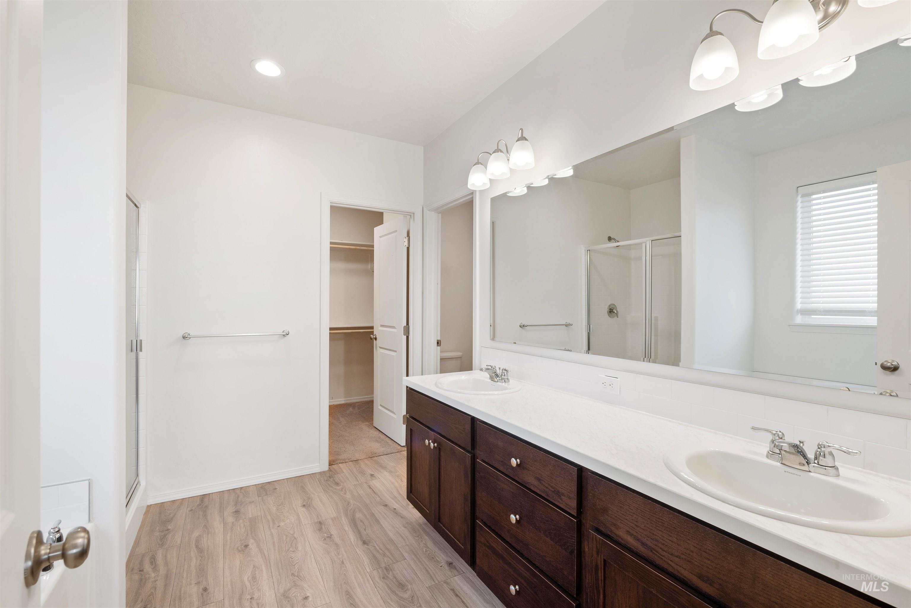 Bathroom featuring a stall shower, light wood finished floors, double vanity, a spacious closet, and recessed lighting