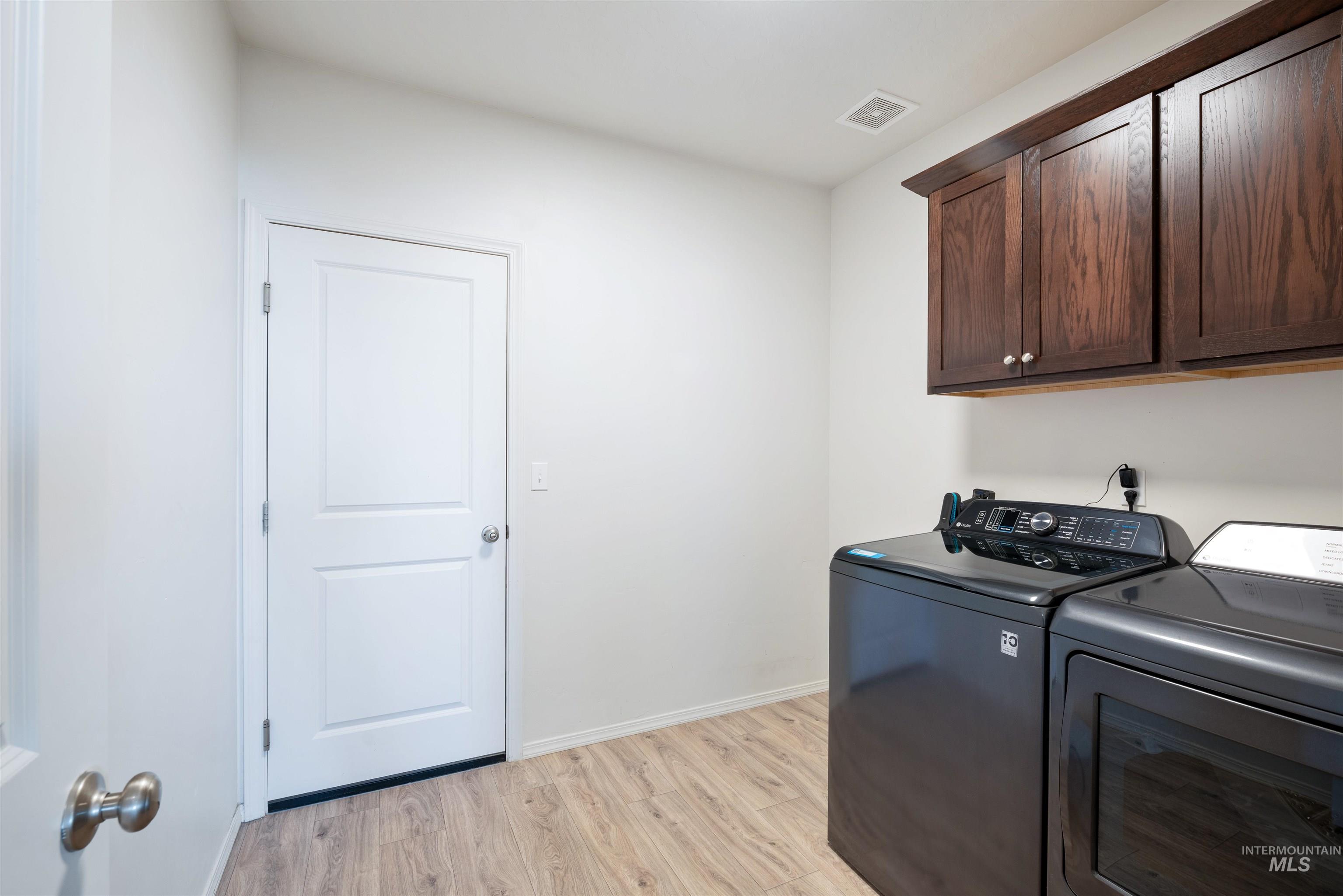 Washroom featuring light wood-style floors, cabinet space, and washing machine and dryer