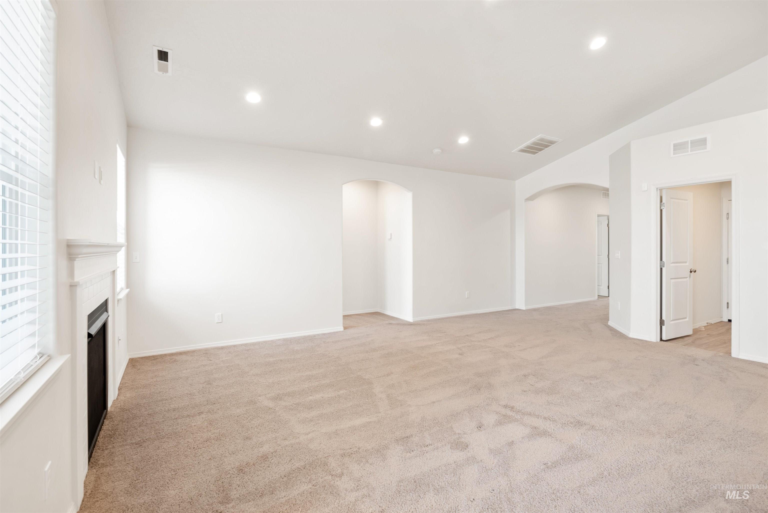 Unfurnished living room featuring recessed lighting, light carpet, a fireplace, arched walkways, and lofted ceiling