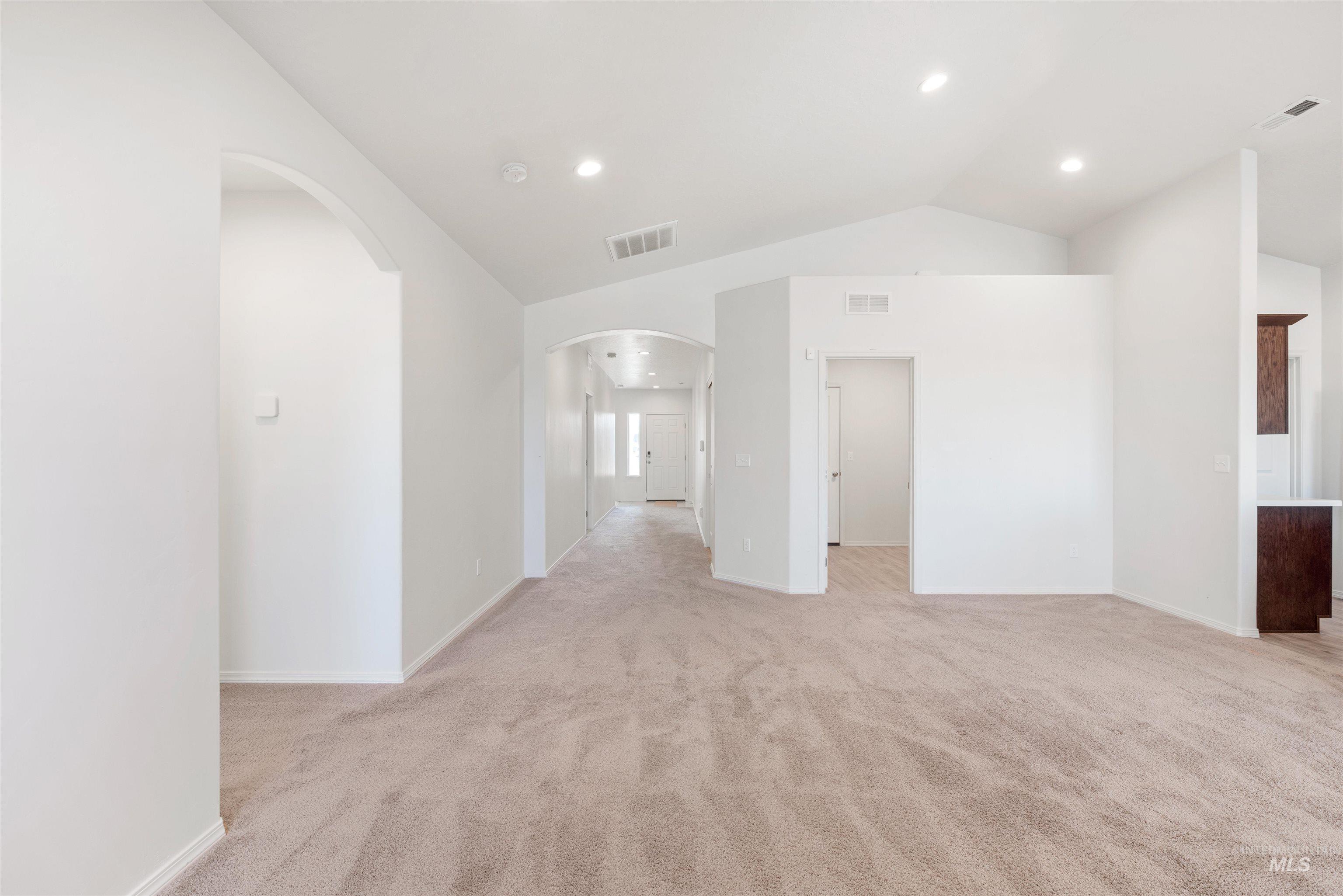Empty room with vaulted ceiling, light colored carpet, recessed lighting, and arched walkways
