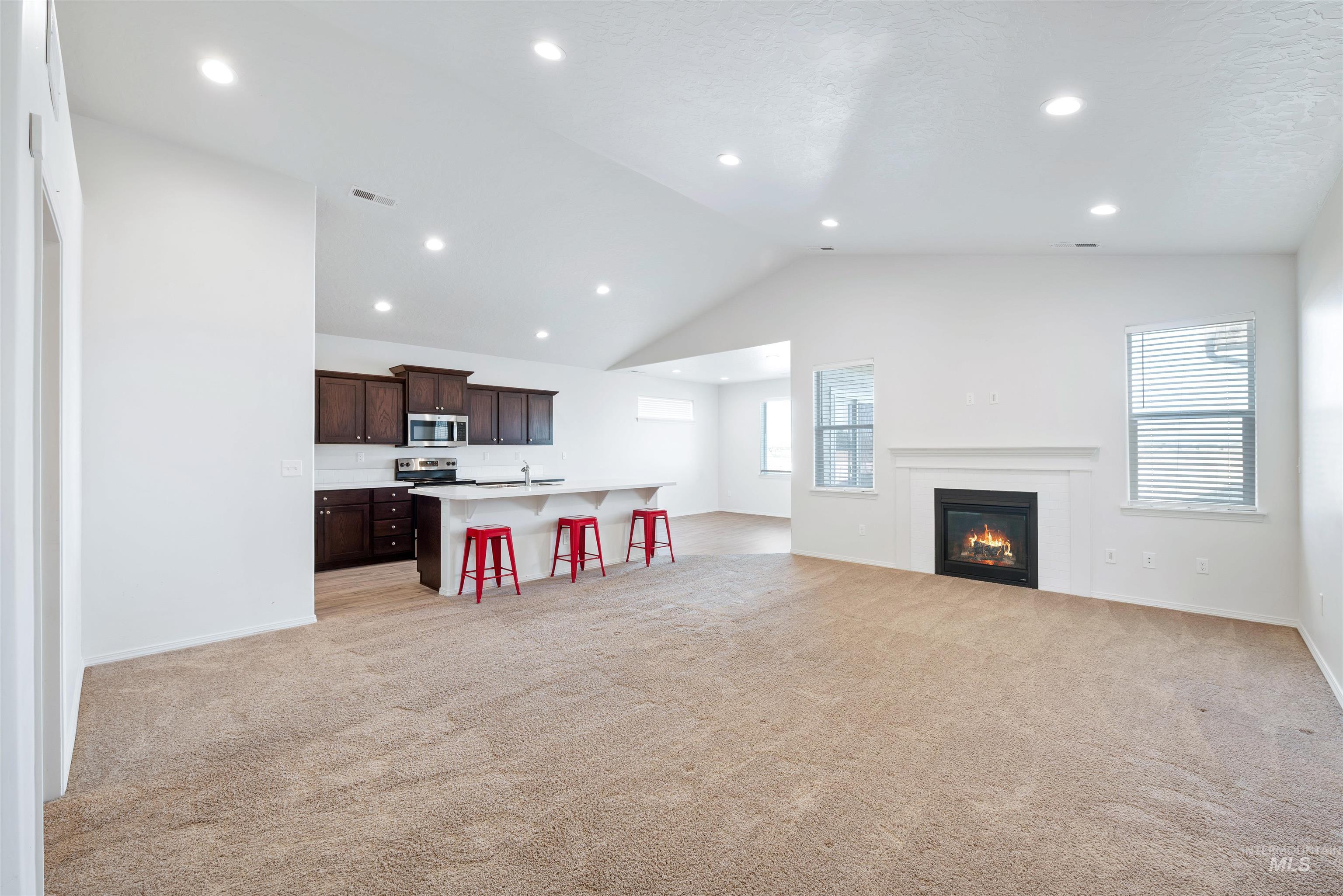 Kitchen featuring a breakfast bar, open floor plan, a glass covered fireplace, dark brown cabinetry, and light colored carpet
