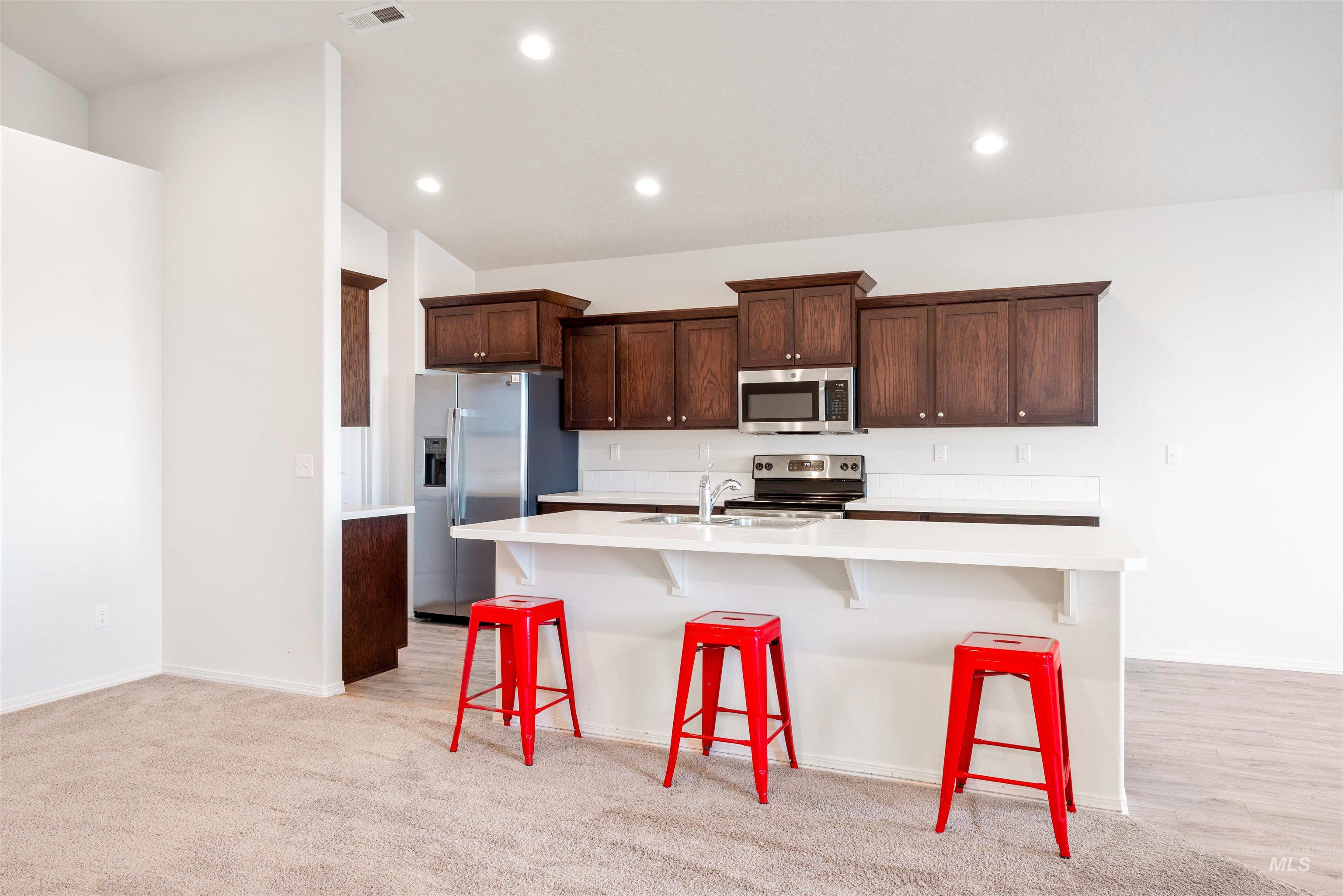 Kitchen with a breakfast bar area, stainless steel appliances, dark brown cabinets, recessed lighting, and a kitchen island with sink
