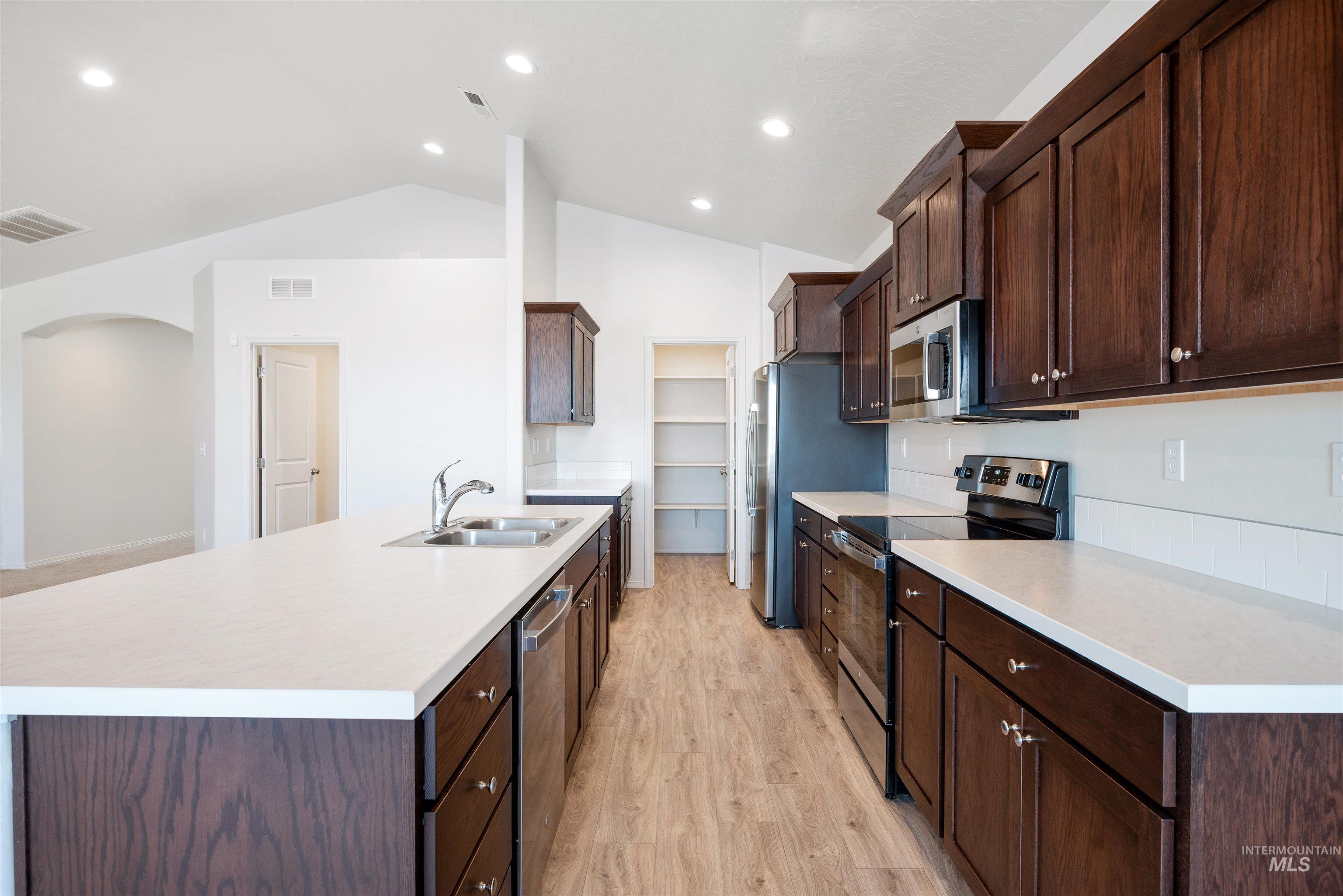 Kitchen with stainless steel appliances, light wood-style floors, lofted ceiling, light countertops, and dark brown cabinets