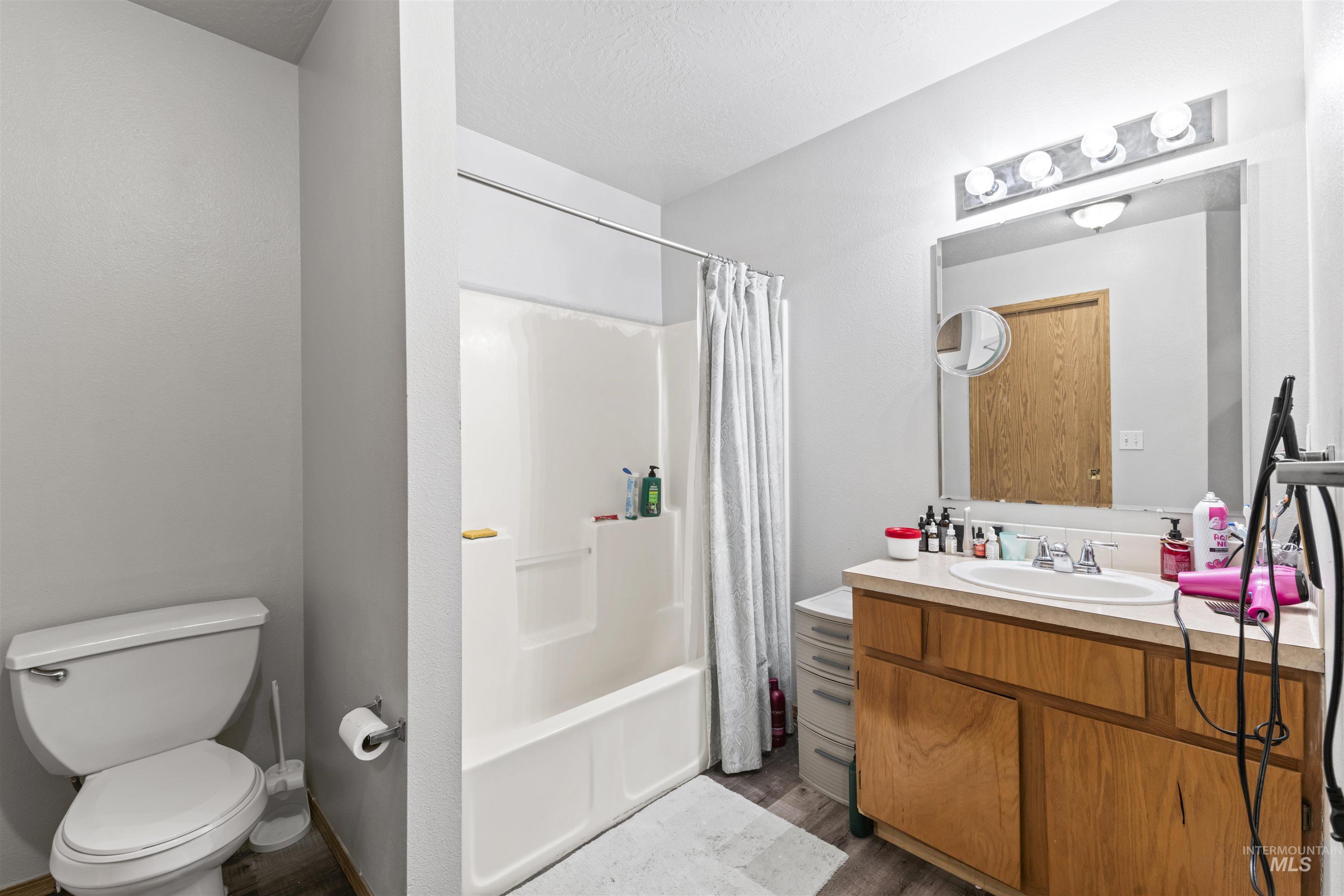 Bathroom with vanity, shower / tub combo, dark wood-style flooring, and a textured ceiling