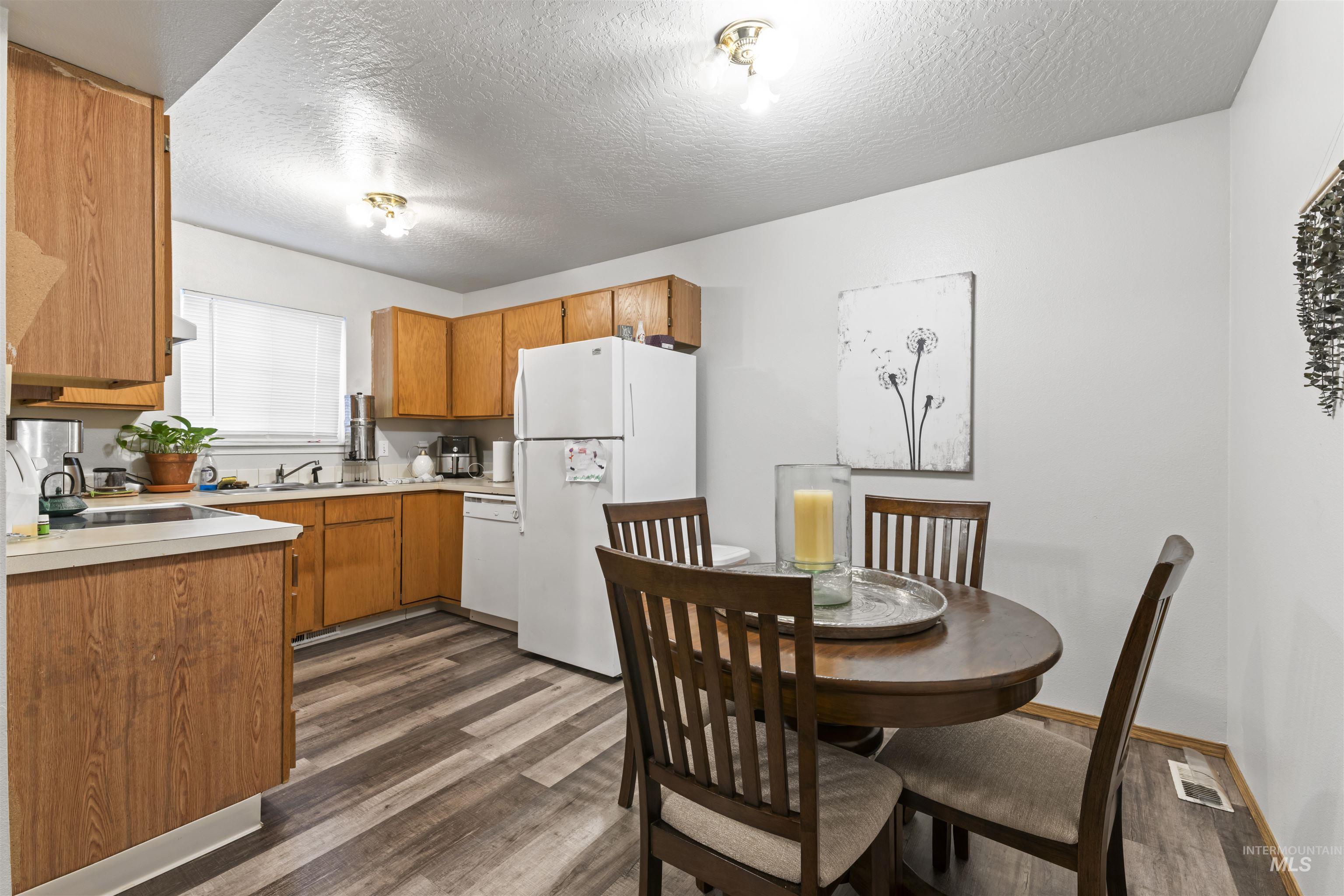 Kitchen with light countertops, white appliances, dark wood-type flooring, brown cabinets, and a textured ceiling