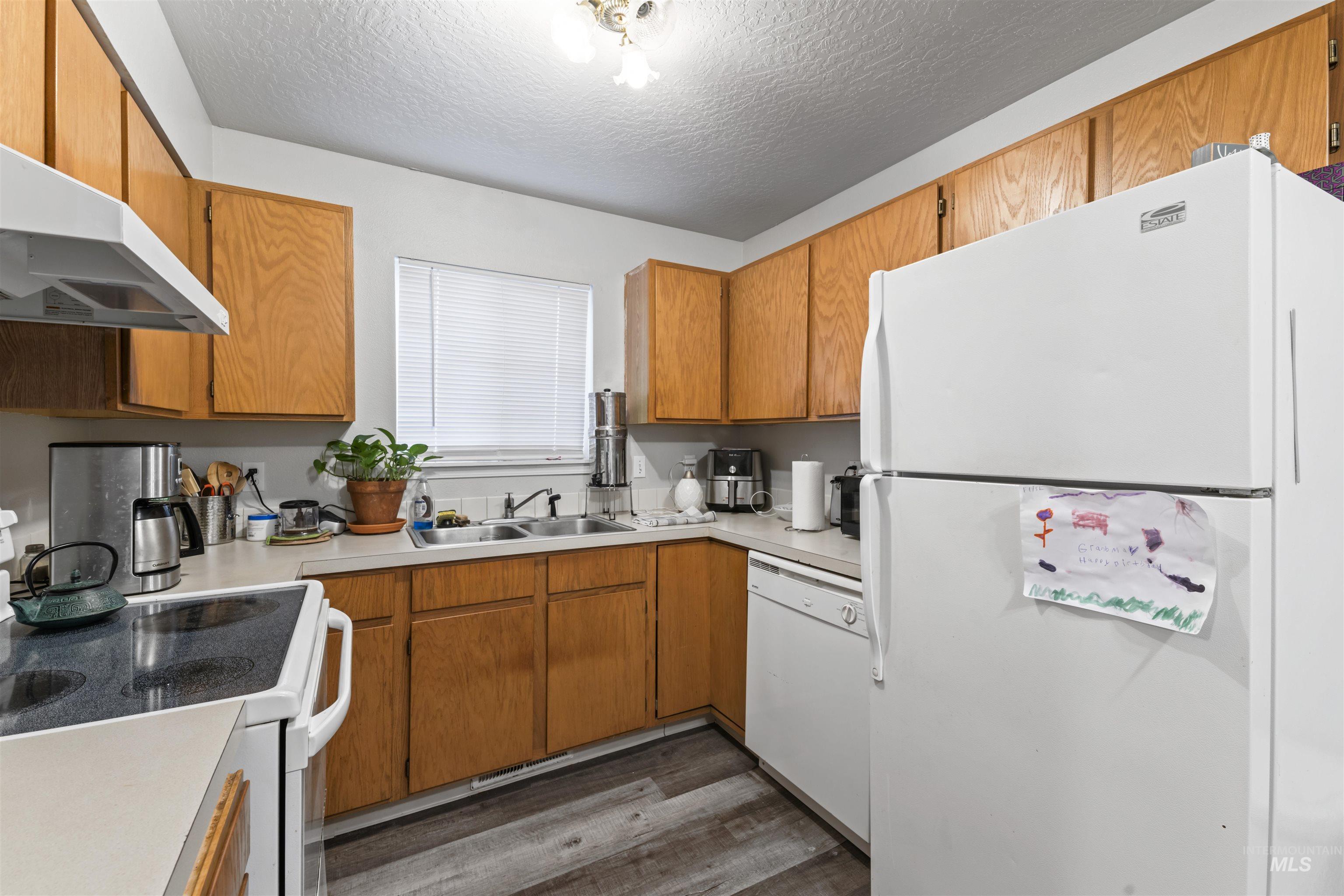 Kitchen featuring white appliances, dark wood finished floors, light countertops, a textured ceiling, and brown cabinetry