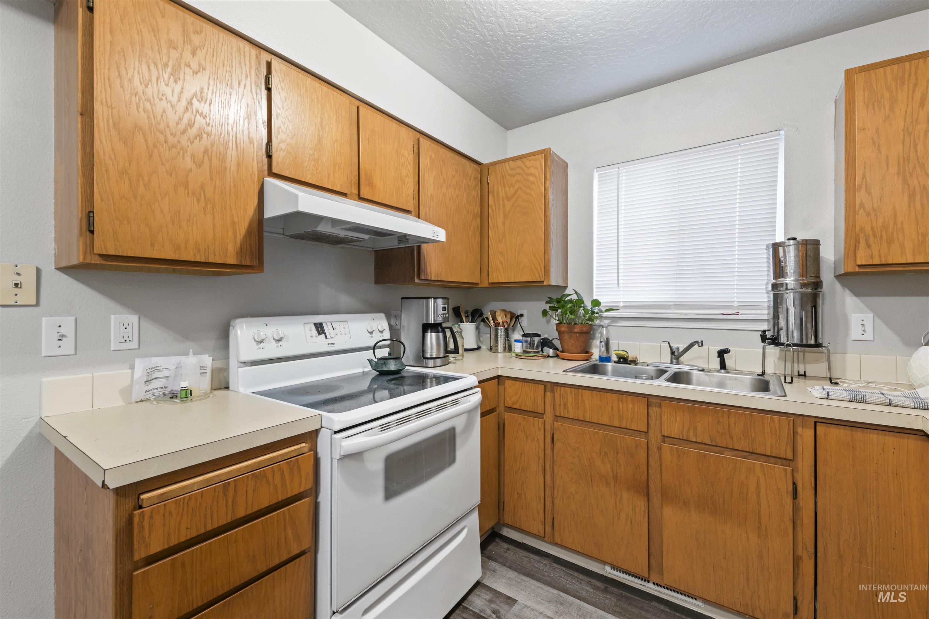 Kitchen featuring electric stove, brown cabinetry, under cabinet range hood, light countertops, and a textured ceiling