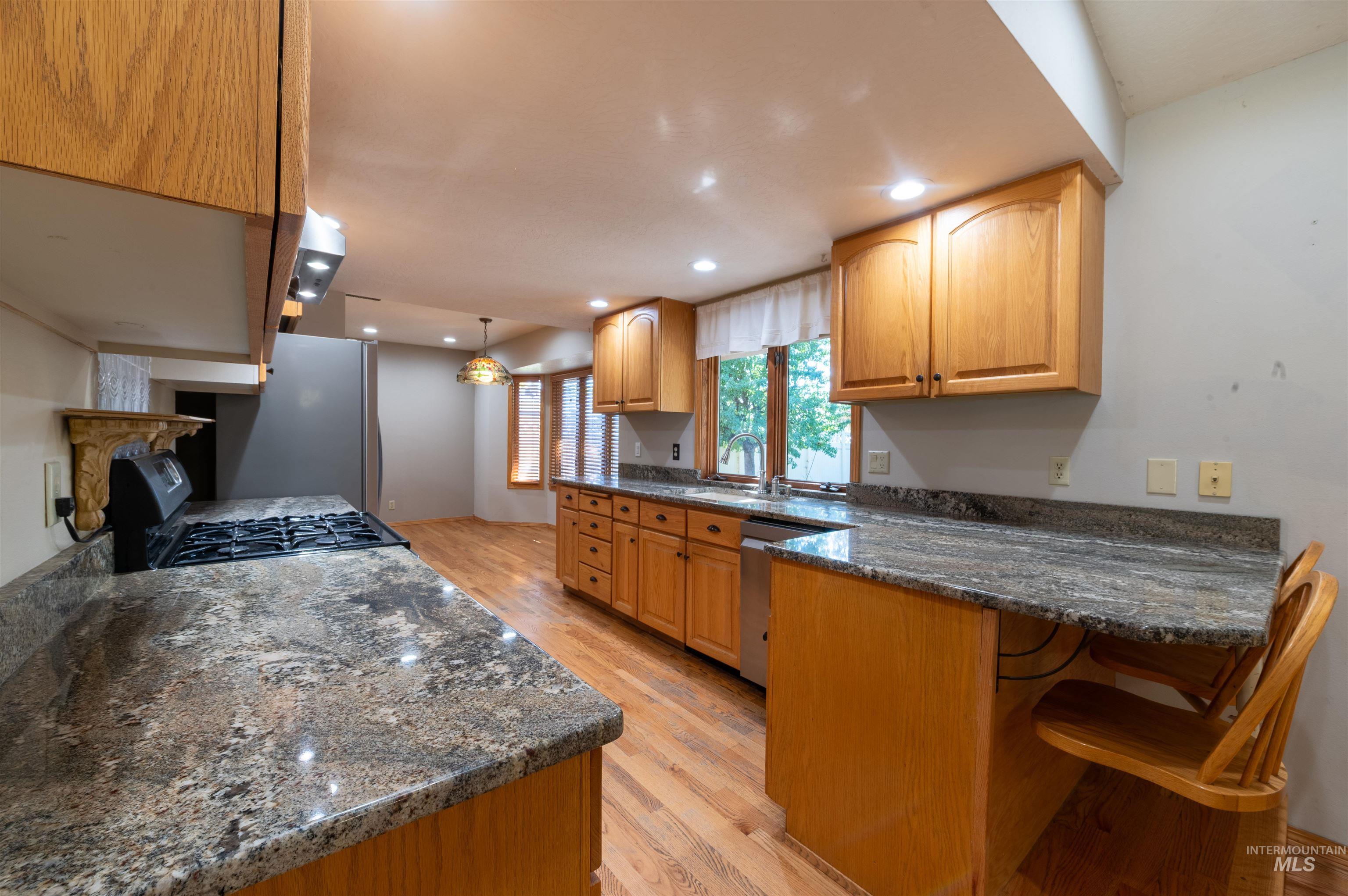 Kitchen featuring light wood-style flooring, pendant lighting, dark stone countertops, a peninsula, and appliances with stainless steel finishes