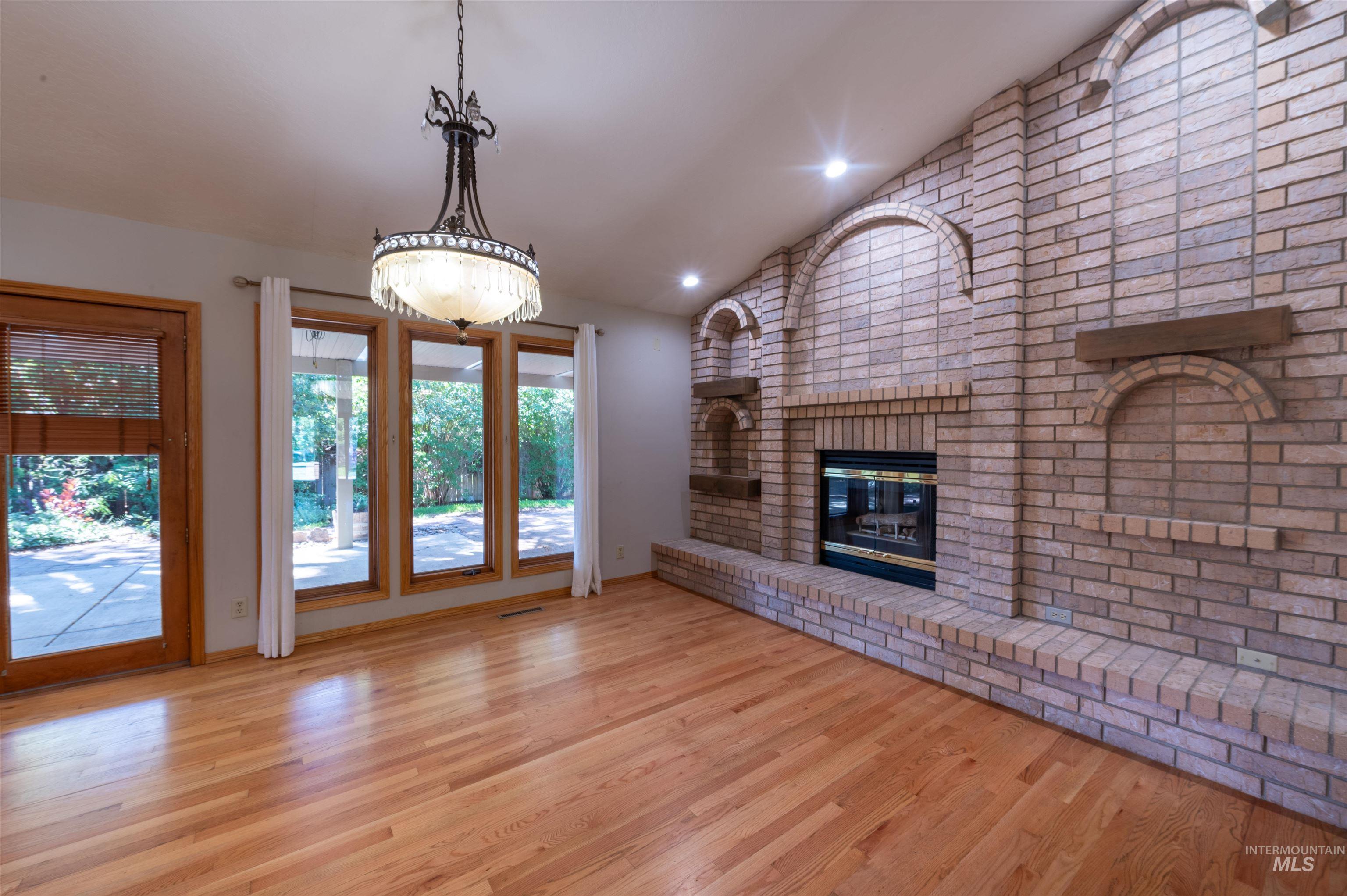 Unfurnished living room featuring lofted ceiling, light wood finished floors, a brick fireplace, and recessed lighting