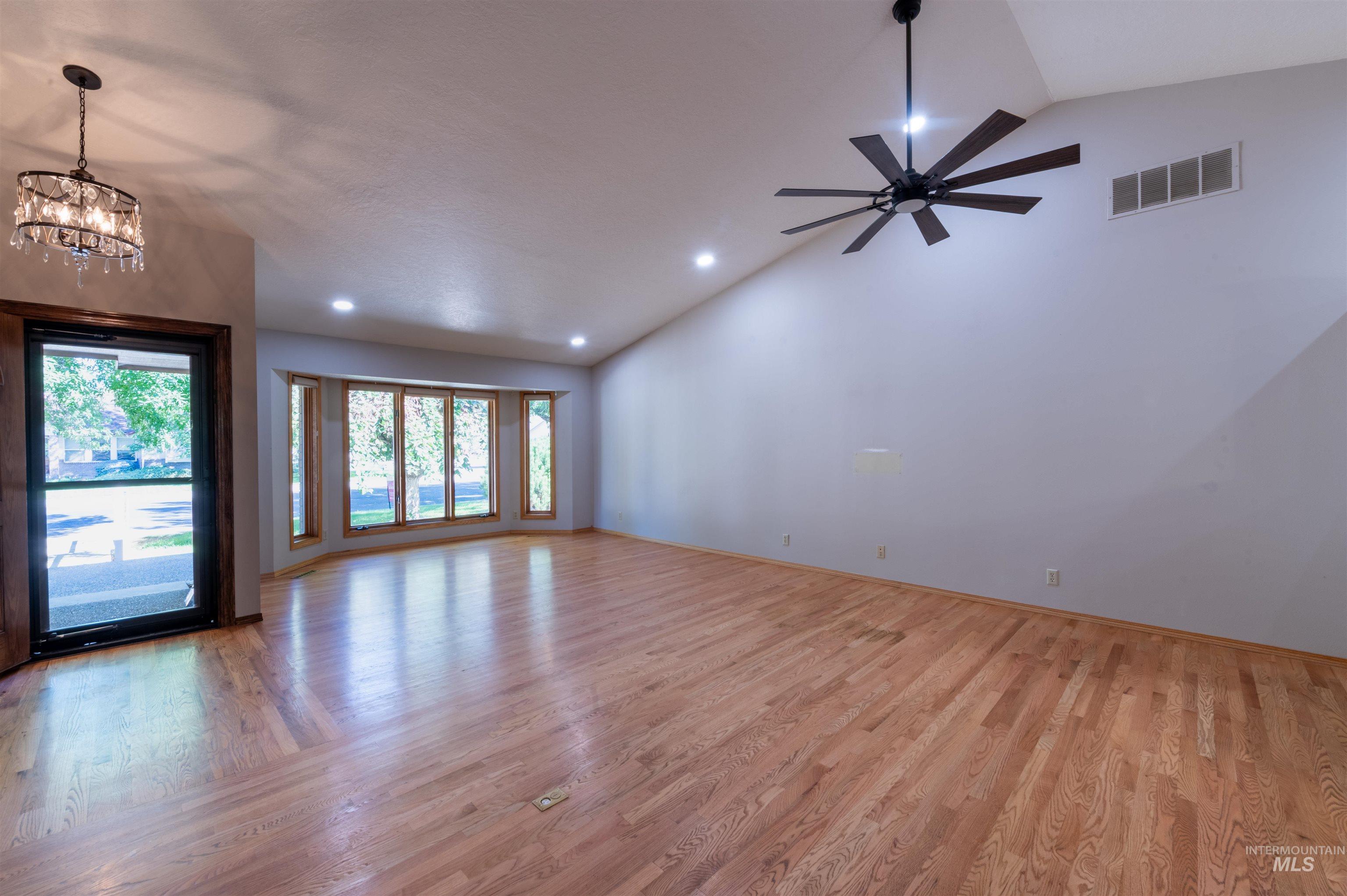Unfurnished living room featuring high vaulted ceiling, light wood-type flooring, recessed lighting, and a chandelier
