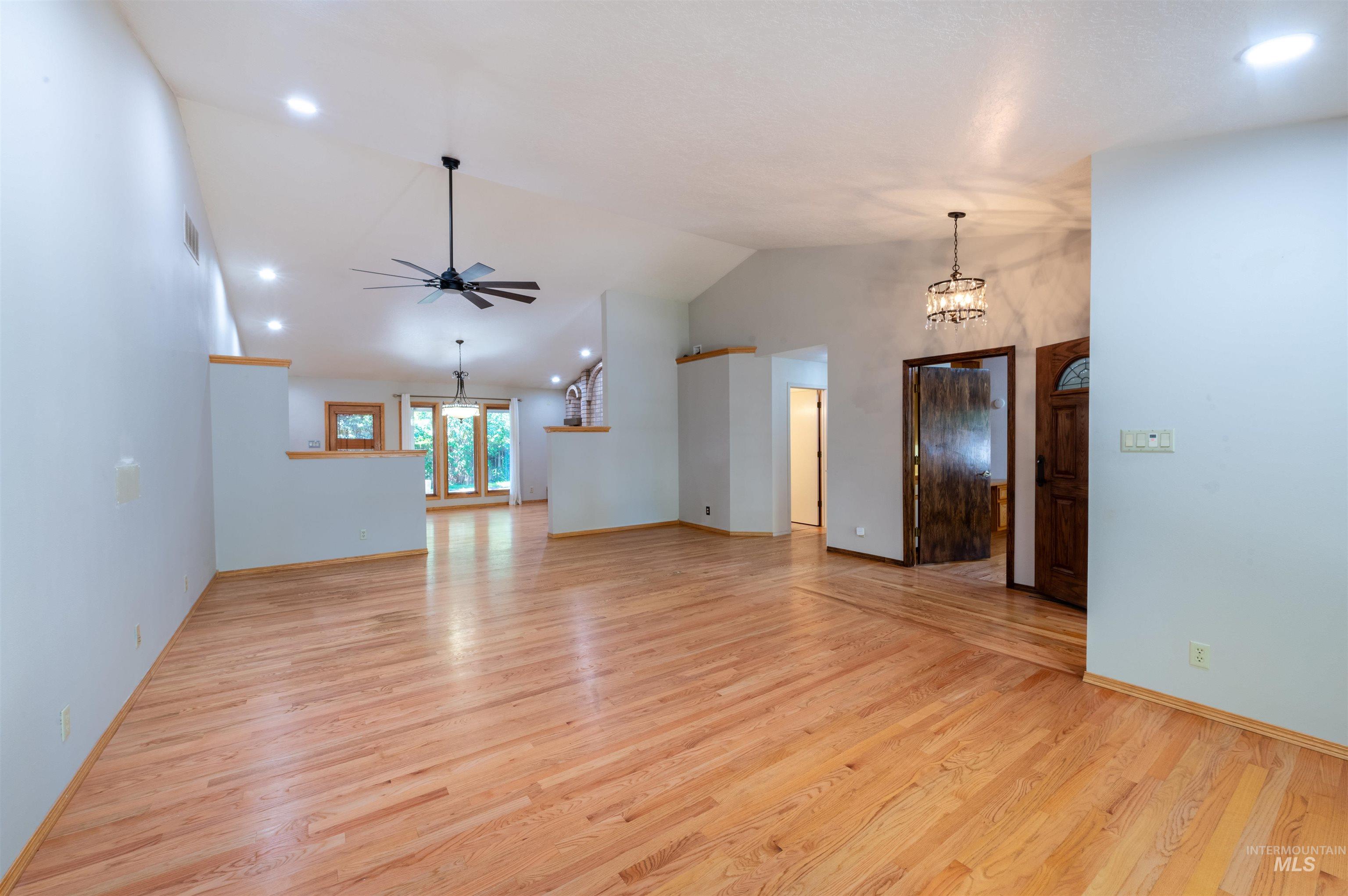 Unfurnished living room featuring recessed lighting, light wood-style flooring, ceiling fan, a chandelier, and high vaulted ceiling