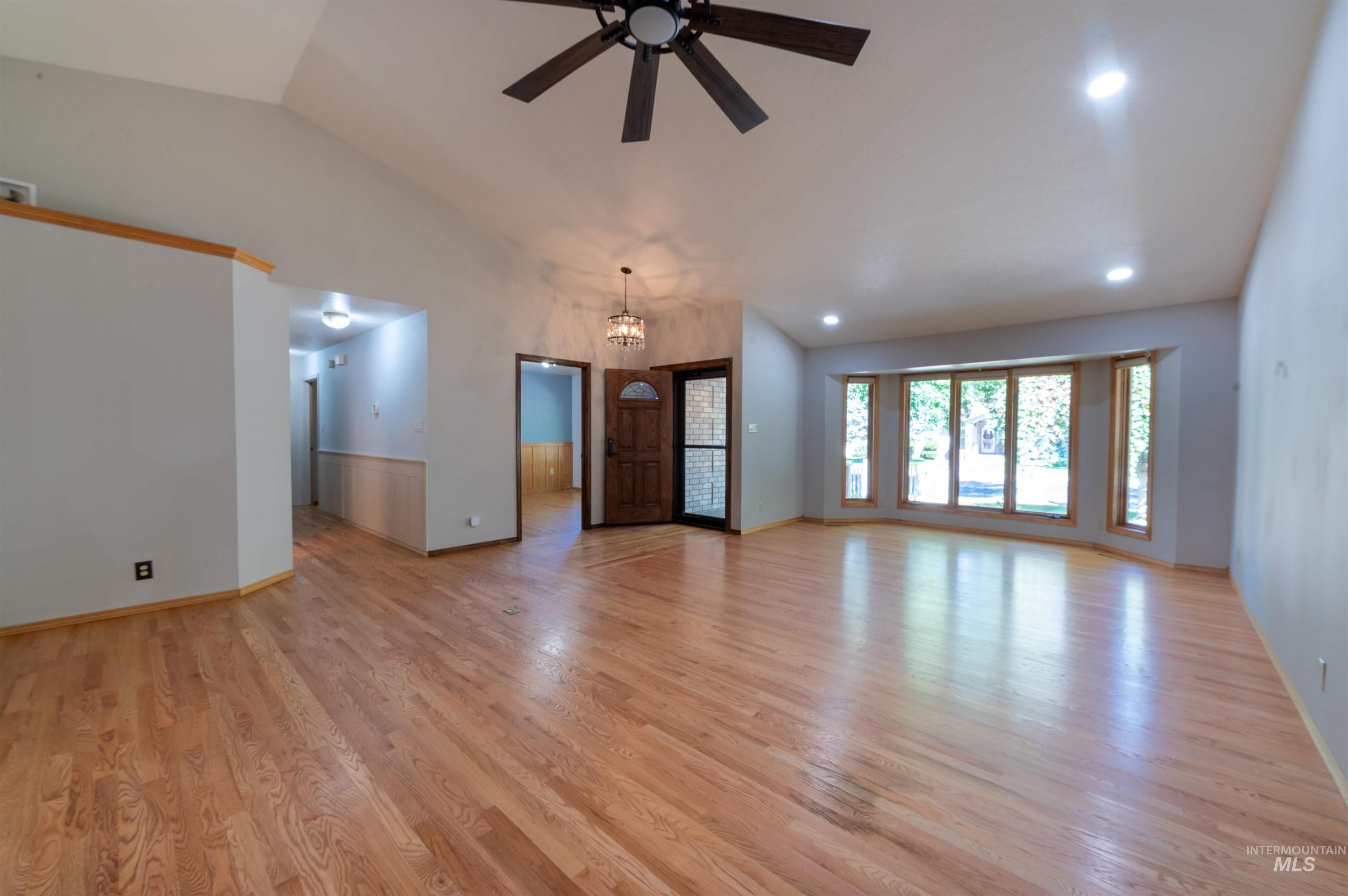 Unfurnished living room with vaulted ceiling, a chandelier, light wood-style flooring, and ceiling fan