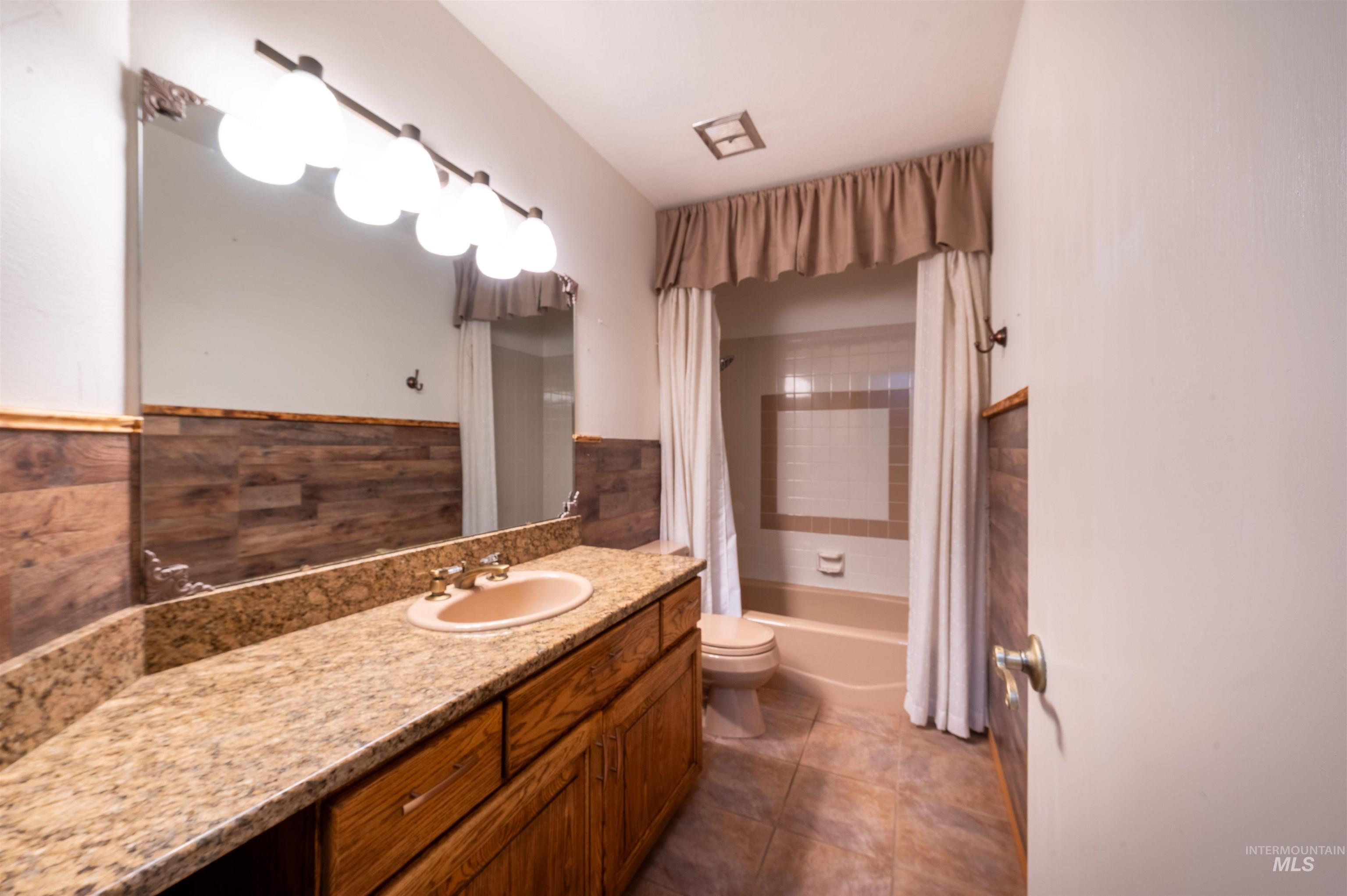 Full bath featuring vanity, shower / bath combo, and dark tile patterned floors