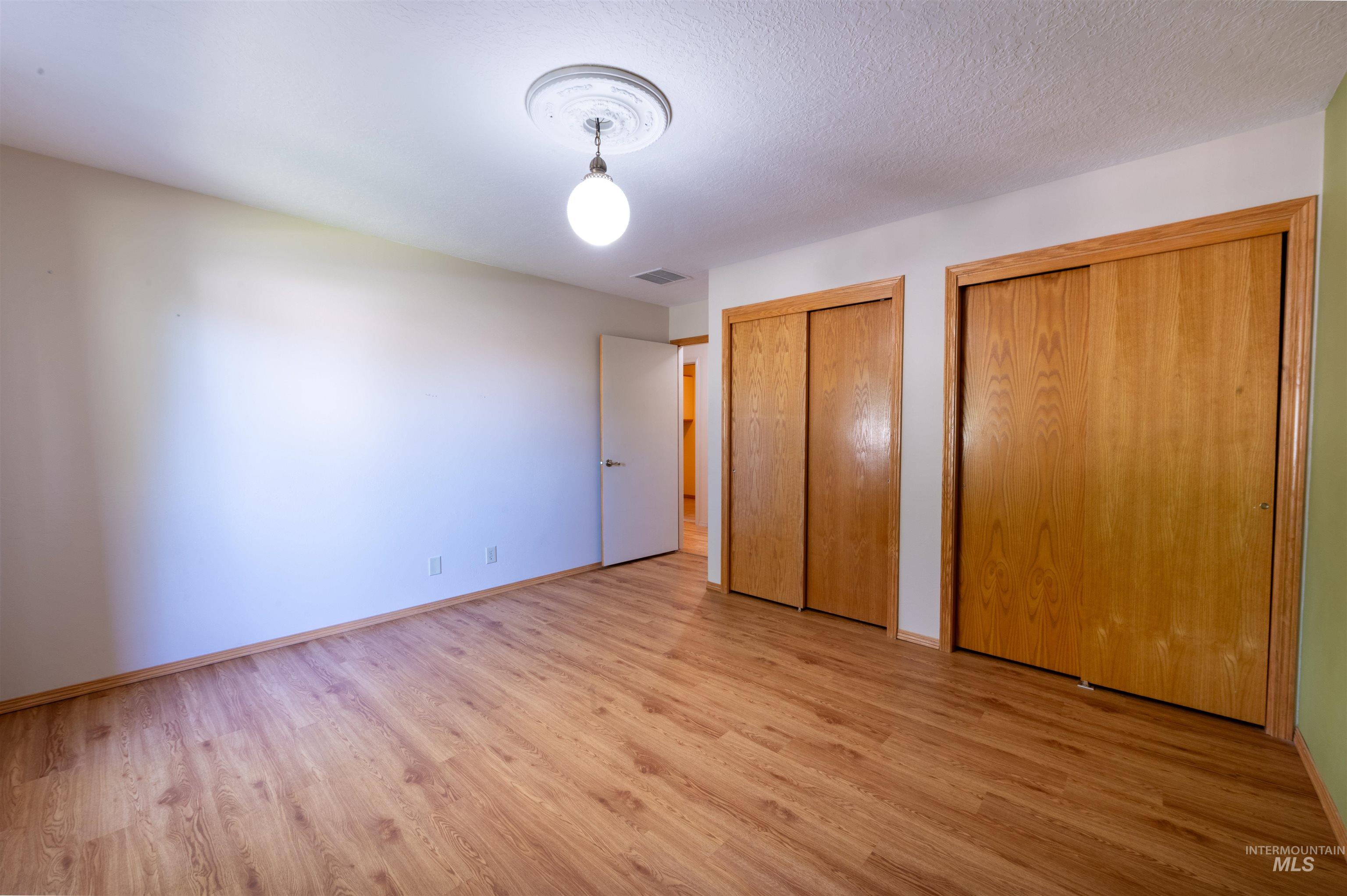 Unfurnished bedroom featuring two closets, light wood-style floors, and a textured ceiling