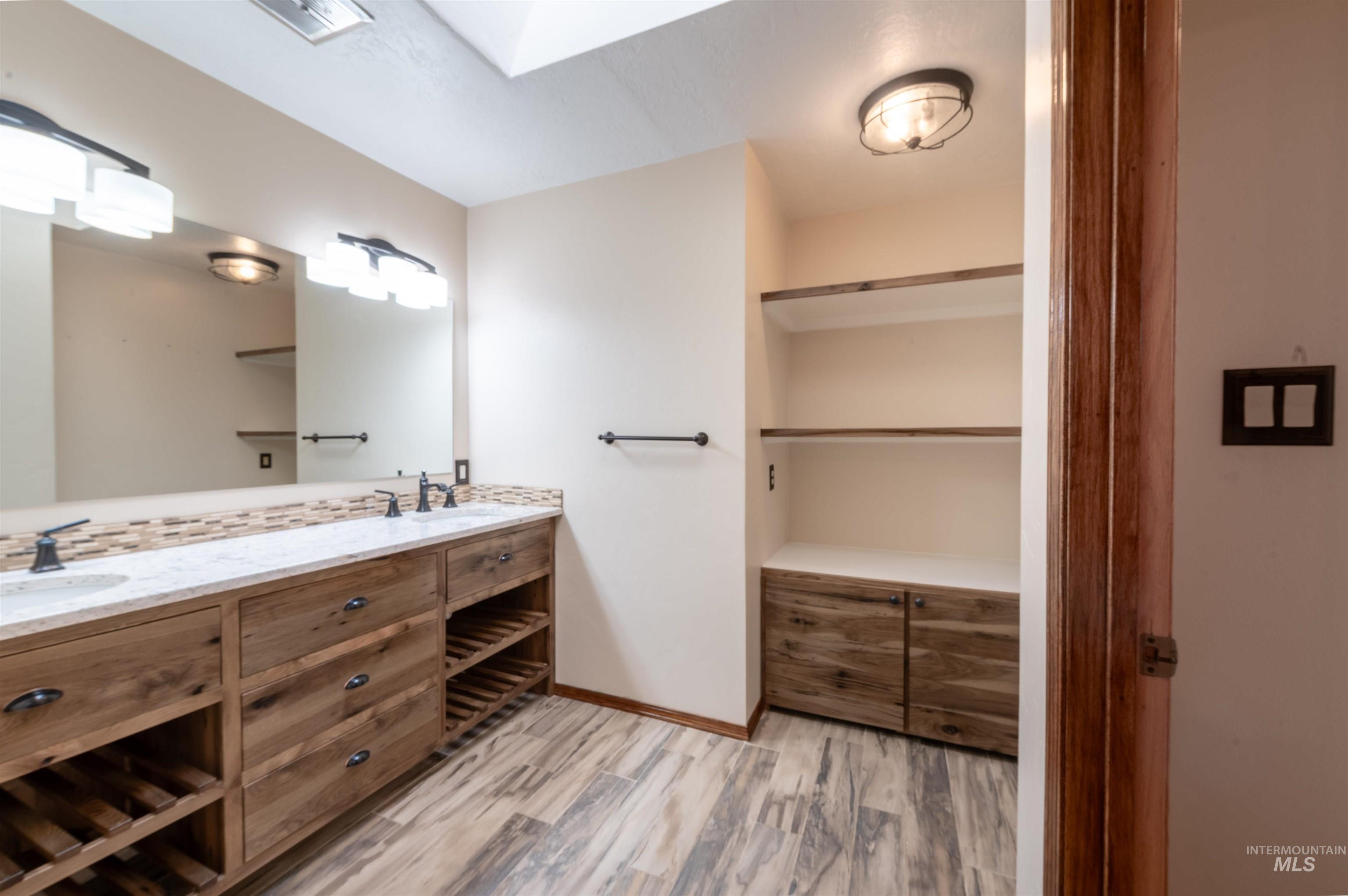 Full bath with double vanity and light wood-style flooring