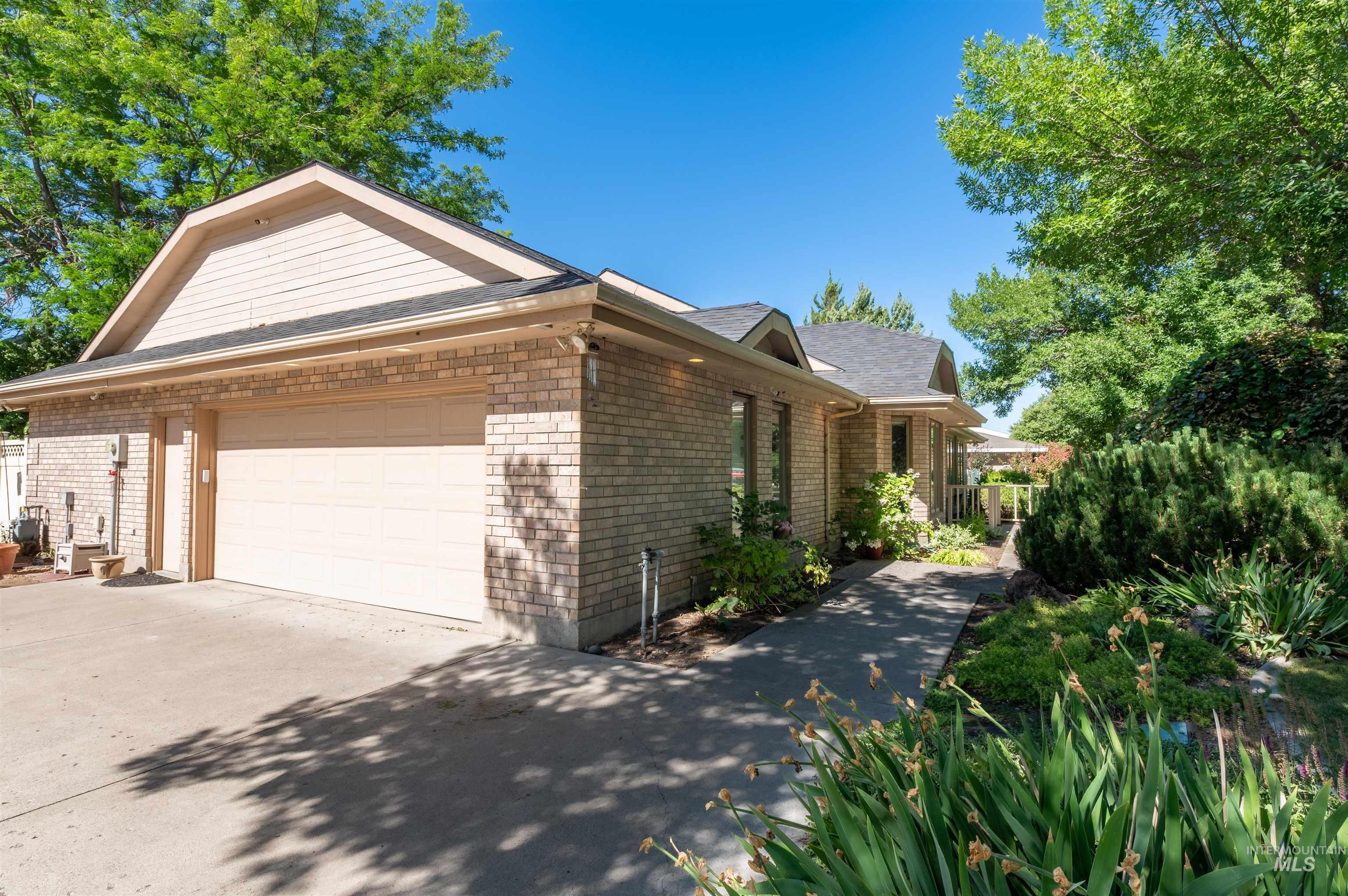 View of property exterior with an attached garage, driveway, brick siding, and a shingled roof